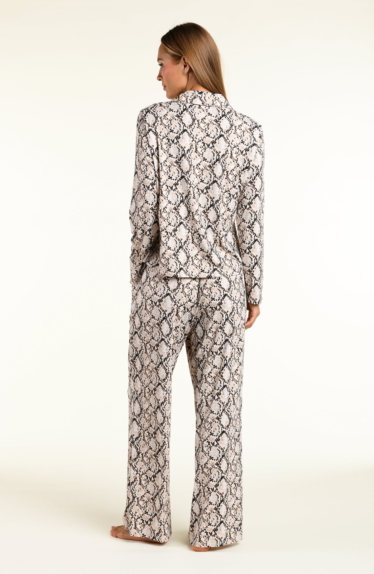 A woman shown from the back wearing a matching long-sleeve top and wide-leg pants set in a beige, black, and white snakeskin pattern, set against a plain off-white studio background.