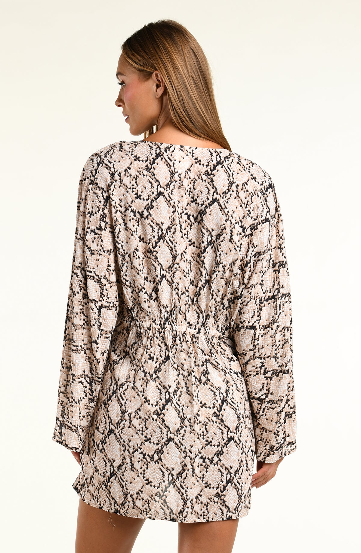 A woman modeling a long-sleeve tunic with a beige, black, and brown snakeskin pattern against a plain light background.