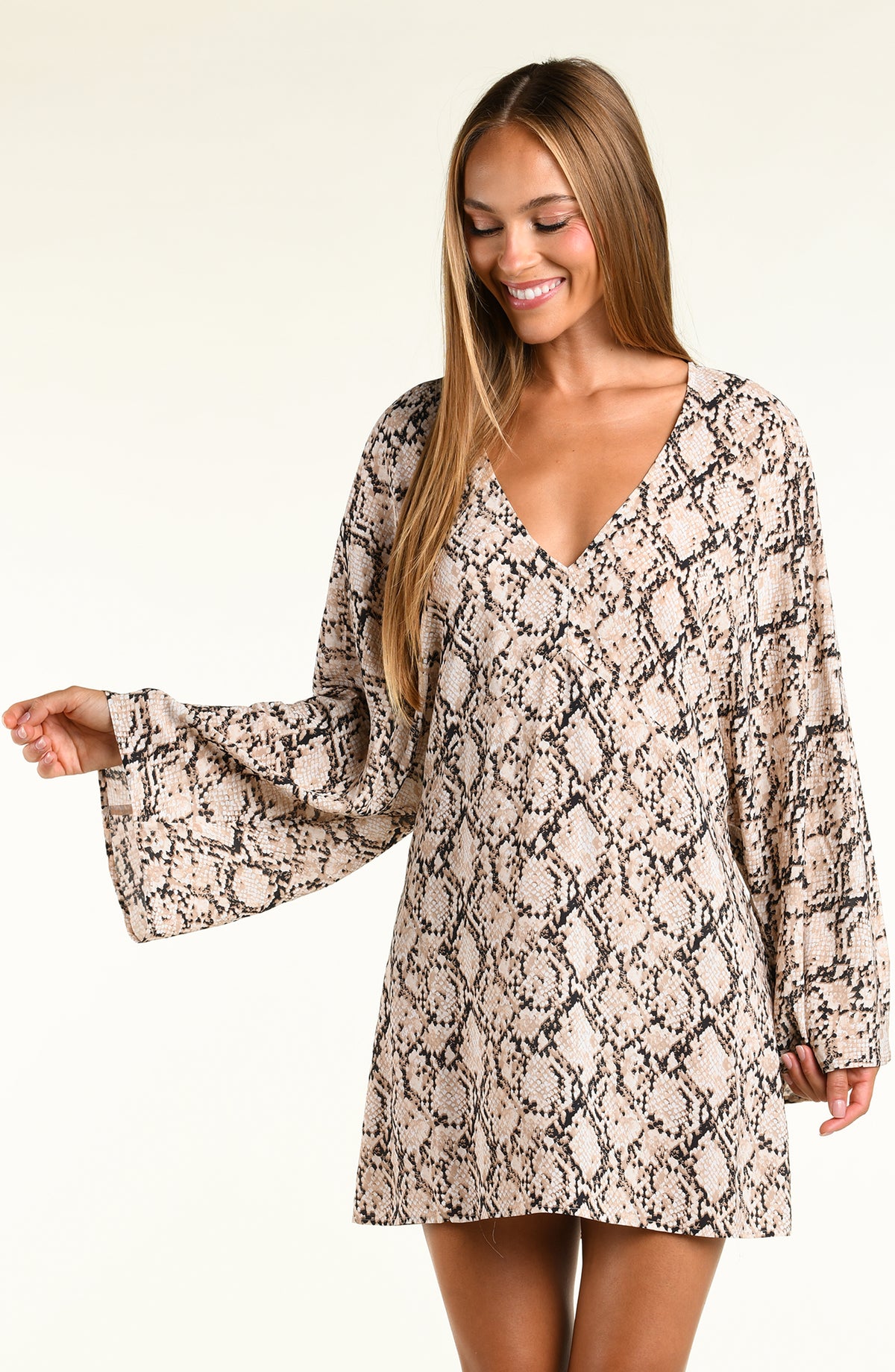 A woman modeling a long-sleeve tunic with a beige, black, and brown snakeskin pattern against a plain light background.