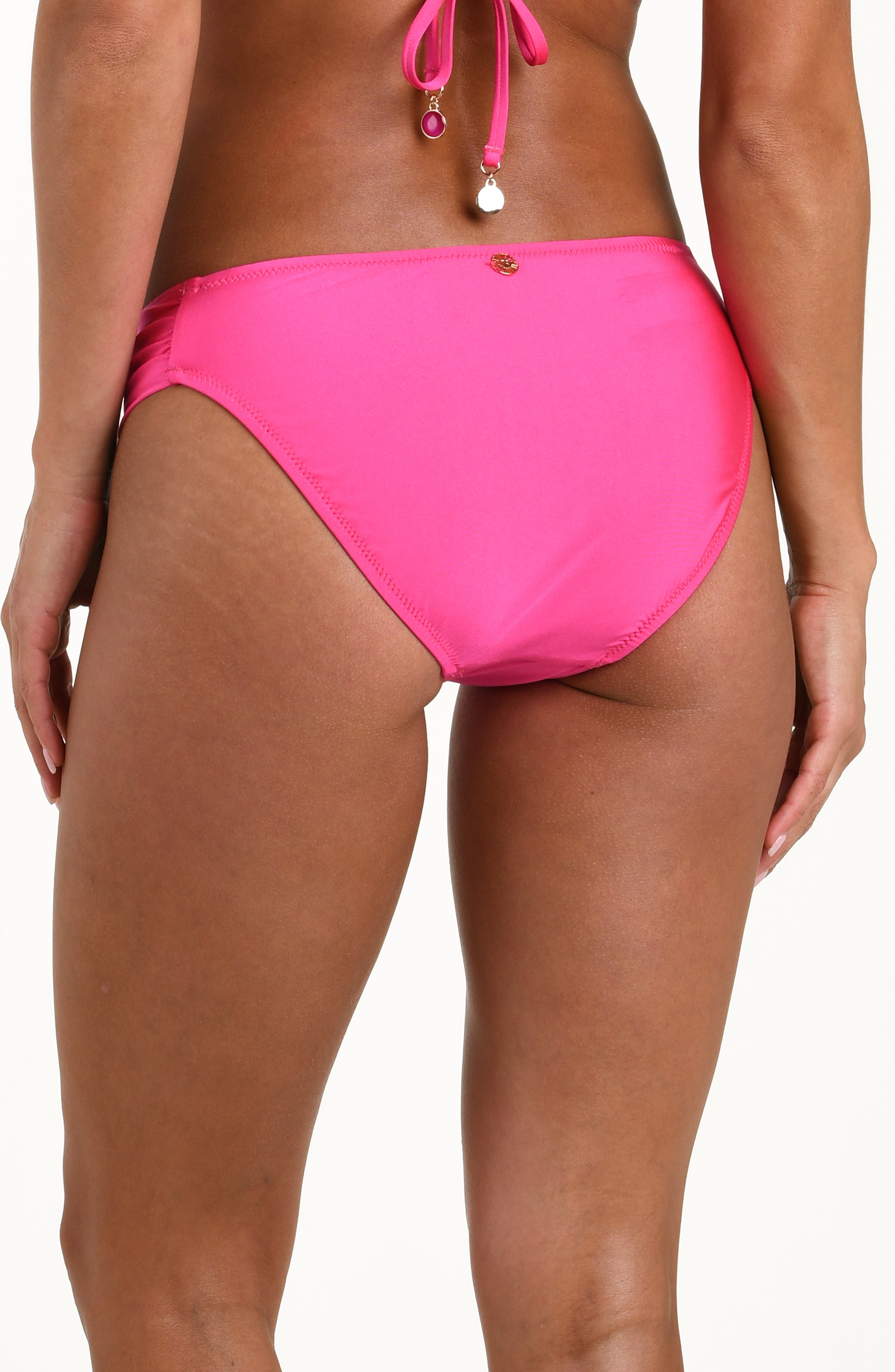 Back image of model wearing a bright pink hipster bikini bottom with shirred sides, gold charm at center, and moderate rear coverage.