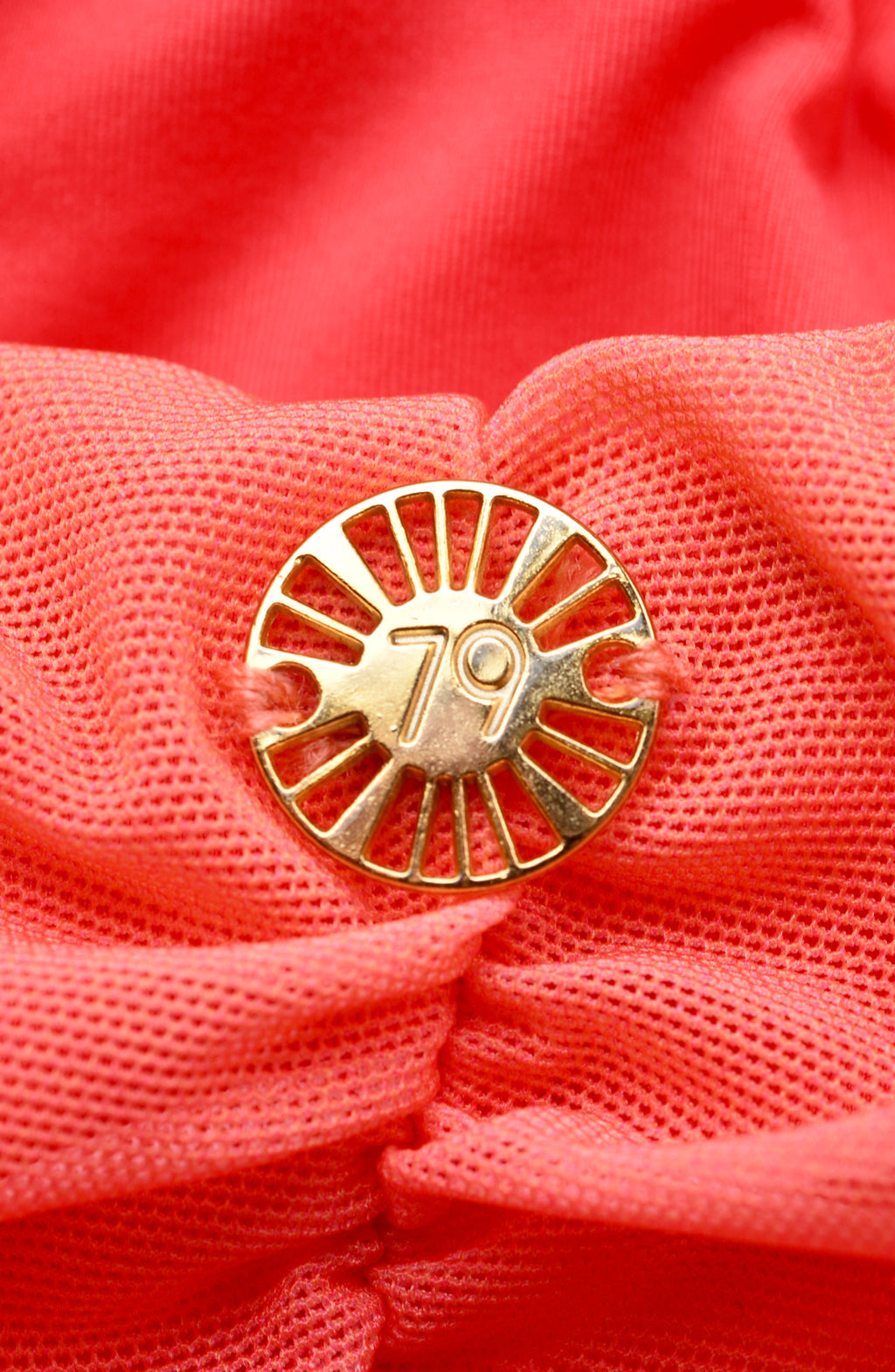 Gold decorative charm with sun design on a pink fabric background