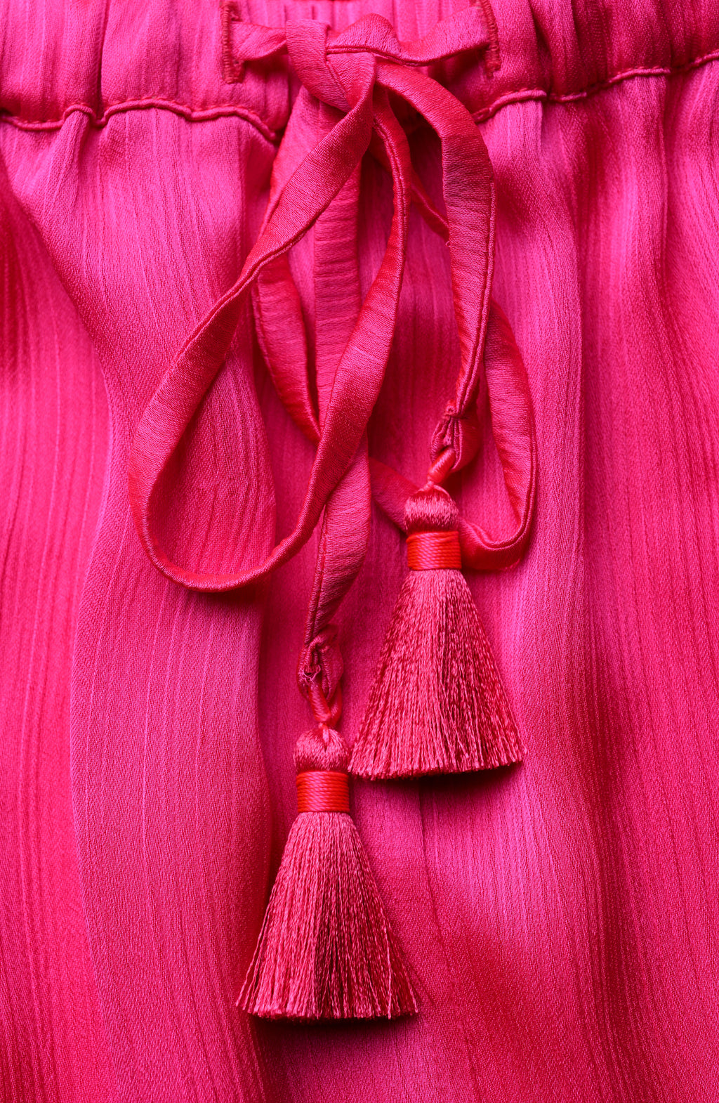 Close-up of a pink fabric with a drawstring waist and tassels on a matching pink background