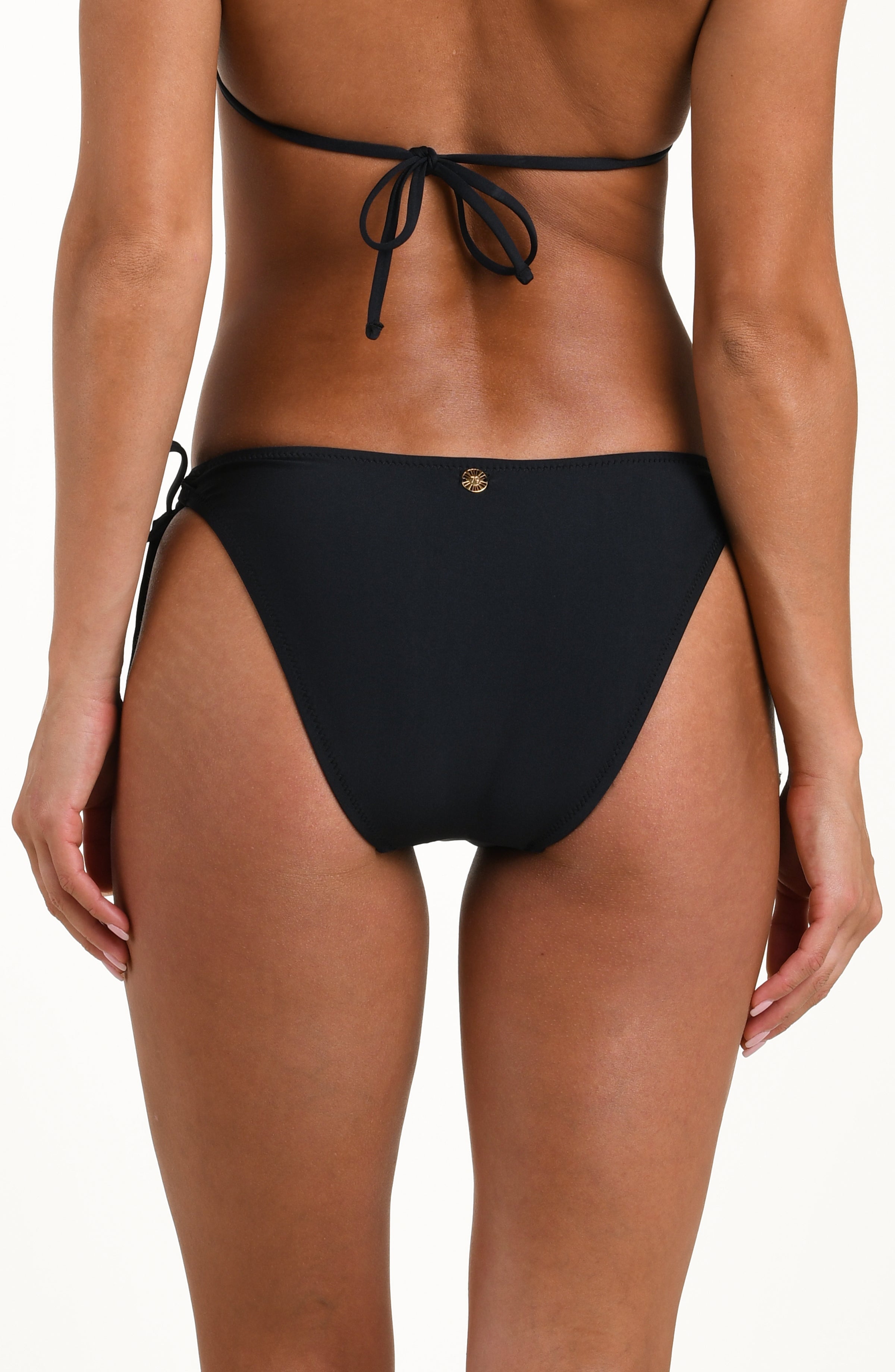 Back image of model wearing solid black bikini bottoms with adjustable side  ties featuring gold dipped ends, a gold charm at center, and contemporary rear coverage.