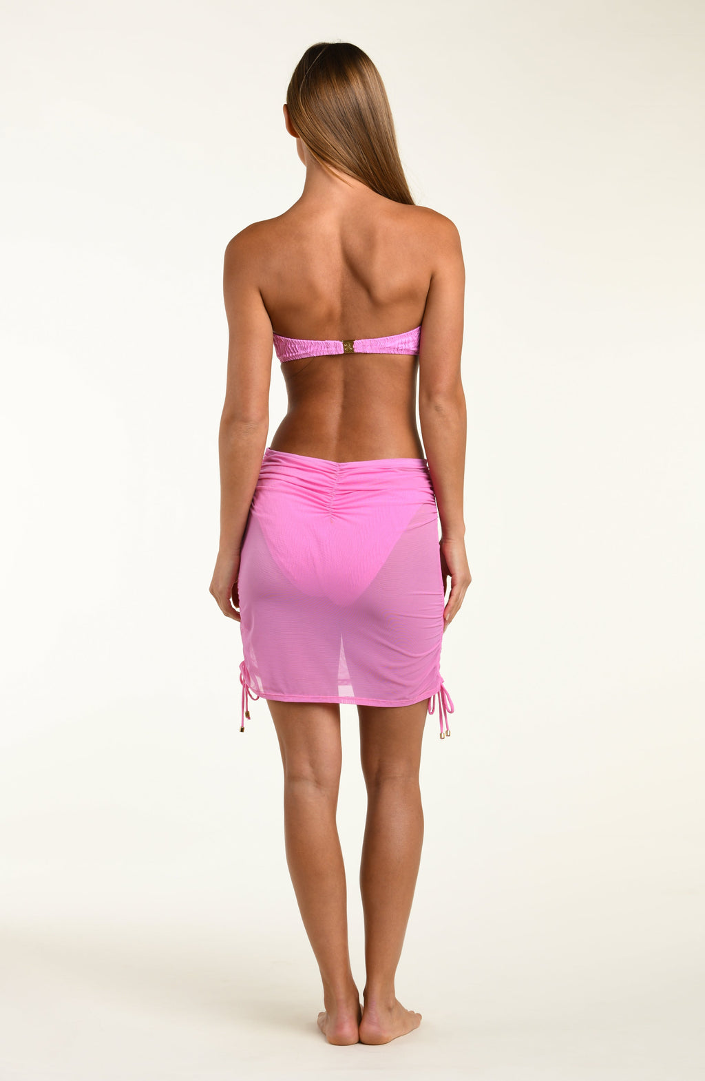 Woman wearing a pink bikini top and matching ruched skirt with drawstrings on a white background