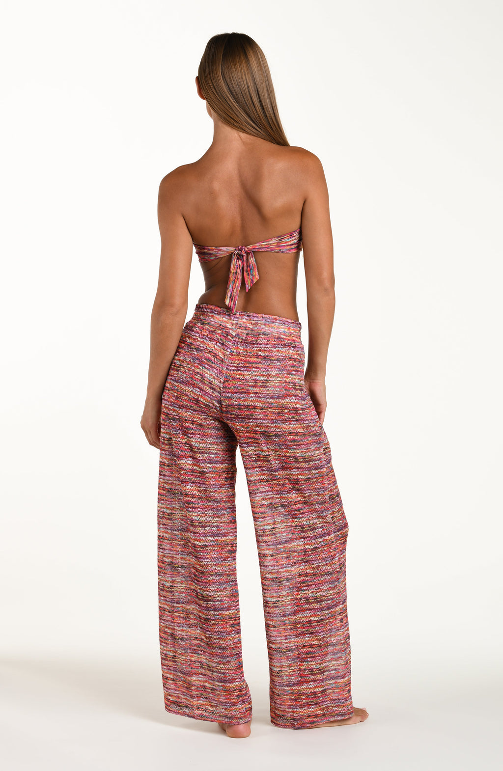 Full body back image of model wearing long beach pants in a multicolored ripple pattern featuring an elastic waist. This is paired with a matching bikini top.