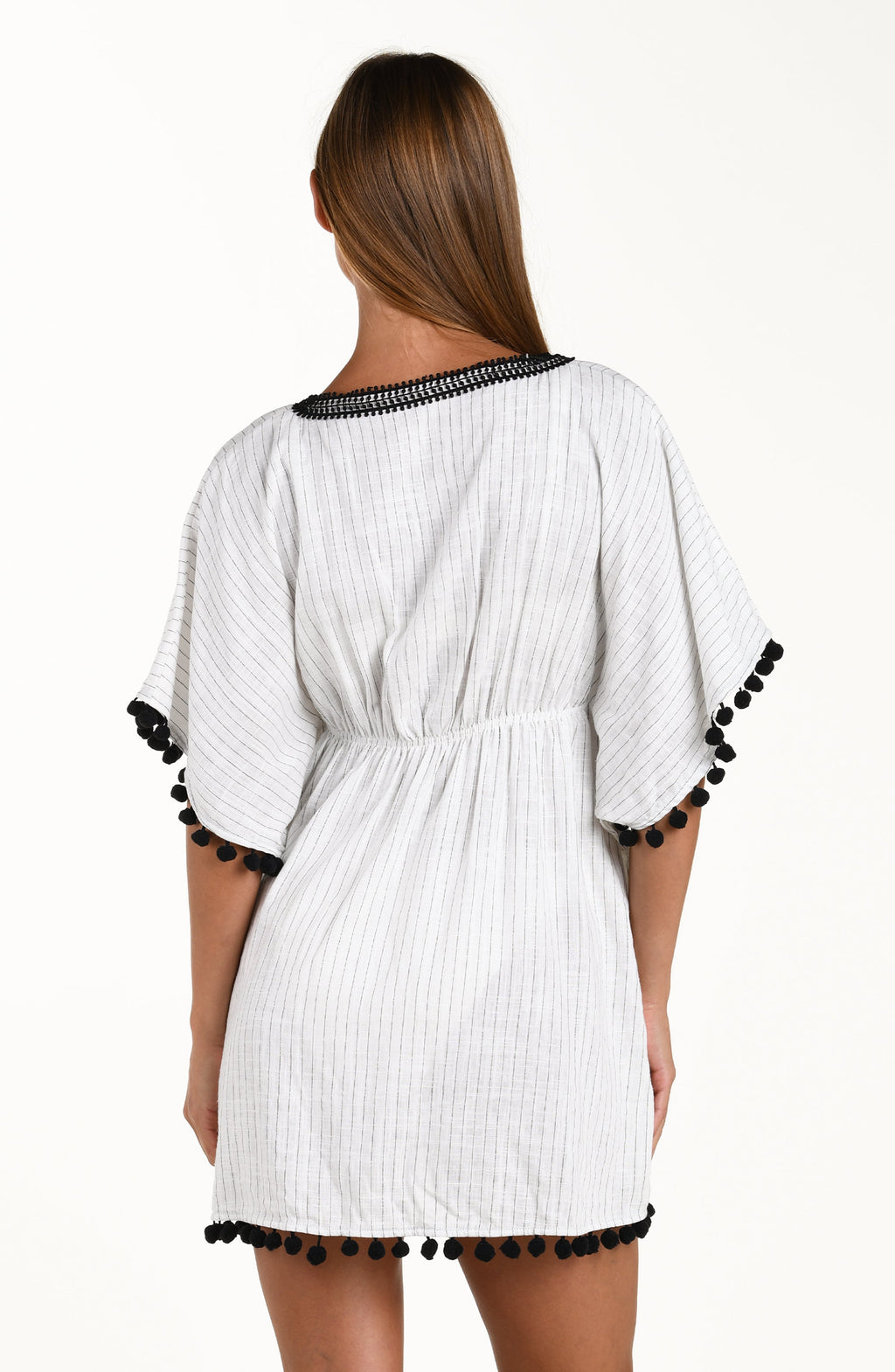 Back image of model wearing a short pull over v-neck caftan with three quarter sleeves adorned with tassel trim. Featuring a cream colored linen print.