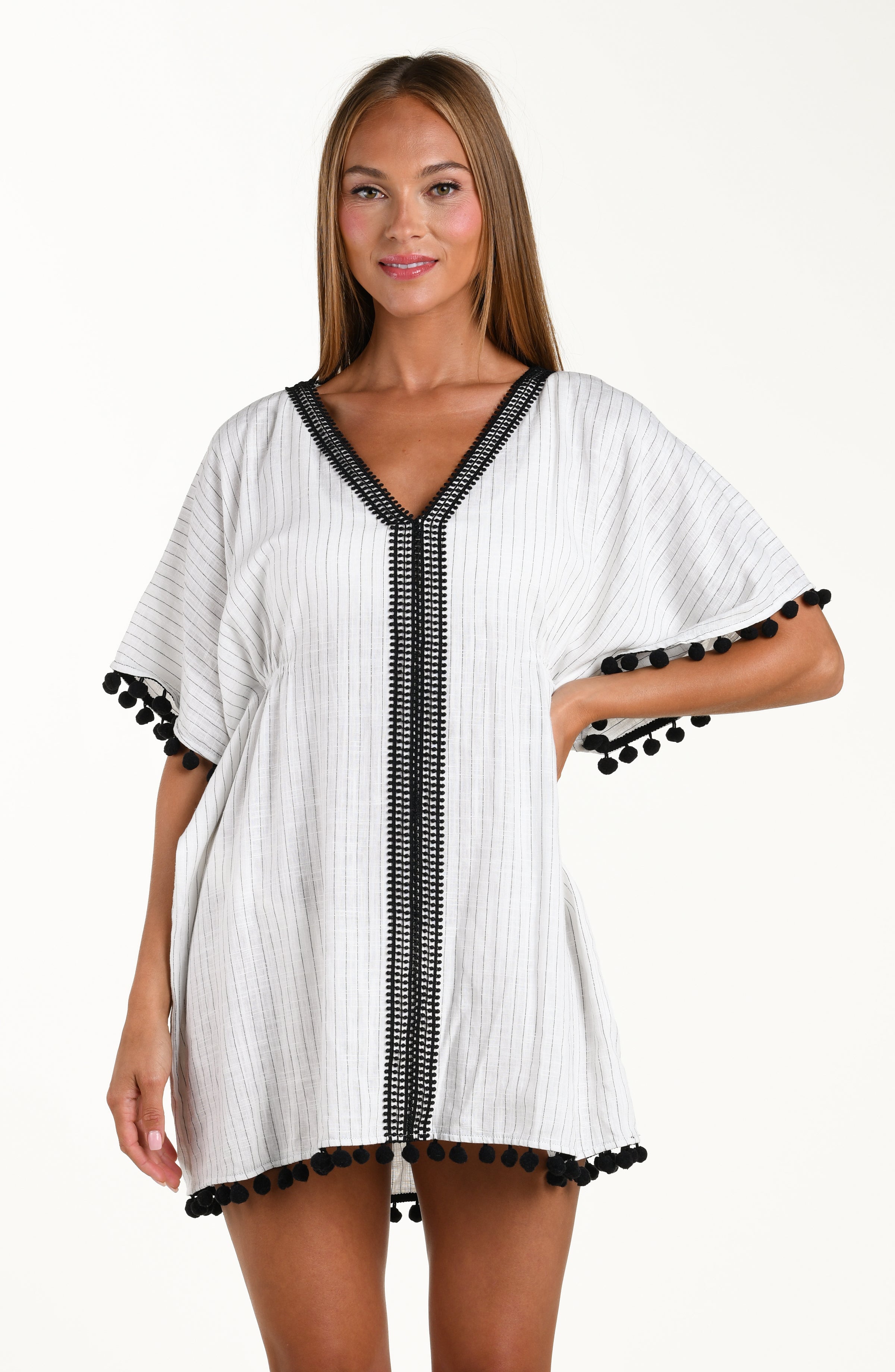 Front image of model wearing a short pull over v-neck caftan with three quarter sleeves adorned with tassel trim. Featuring a cream colored linen print.