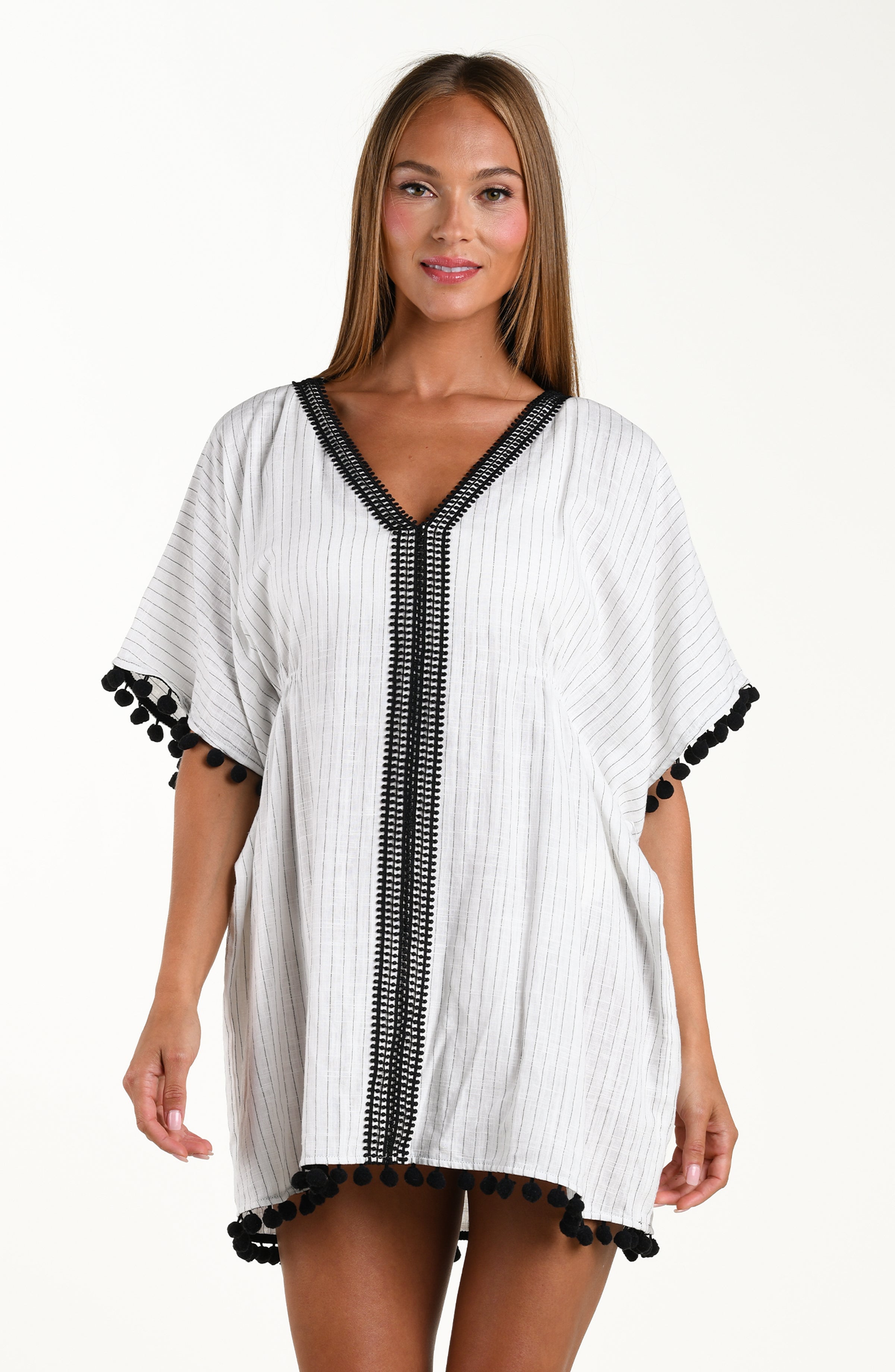 Front image of model wearing a short pull over v-neck caftan with three quarter sleeves adorned with tassel trim. Featuring a cream colored linen print.