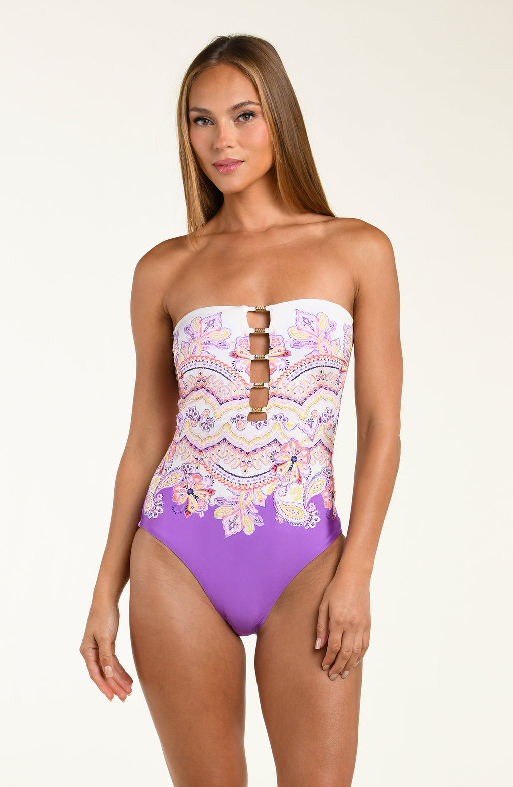Woman wearing a purple and white patterned one piece swimsuit on a plain background