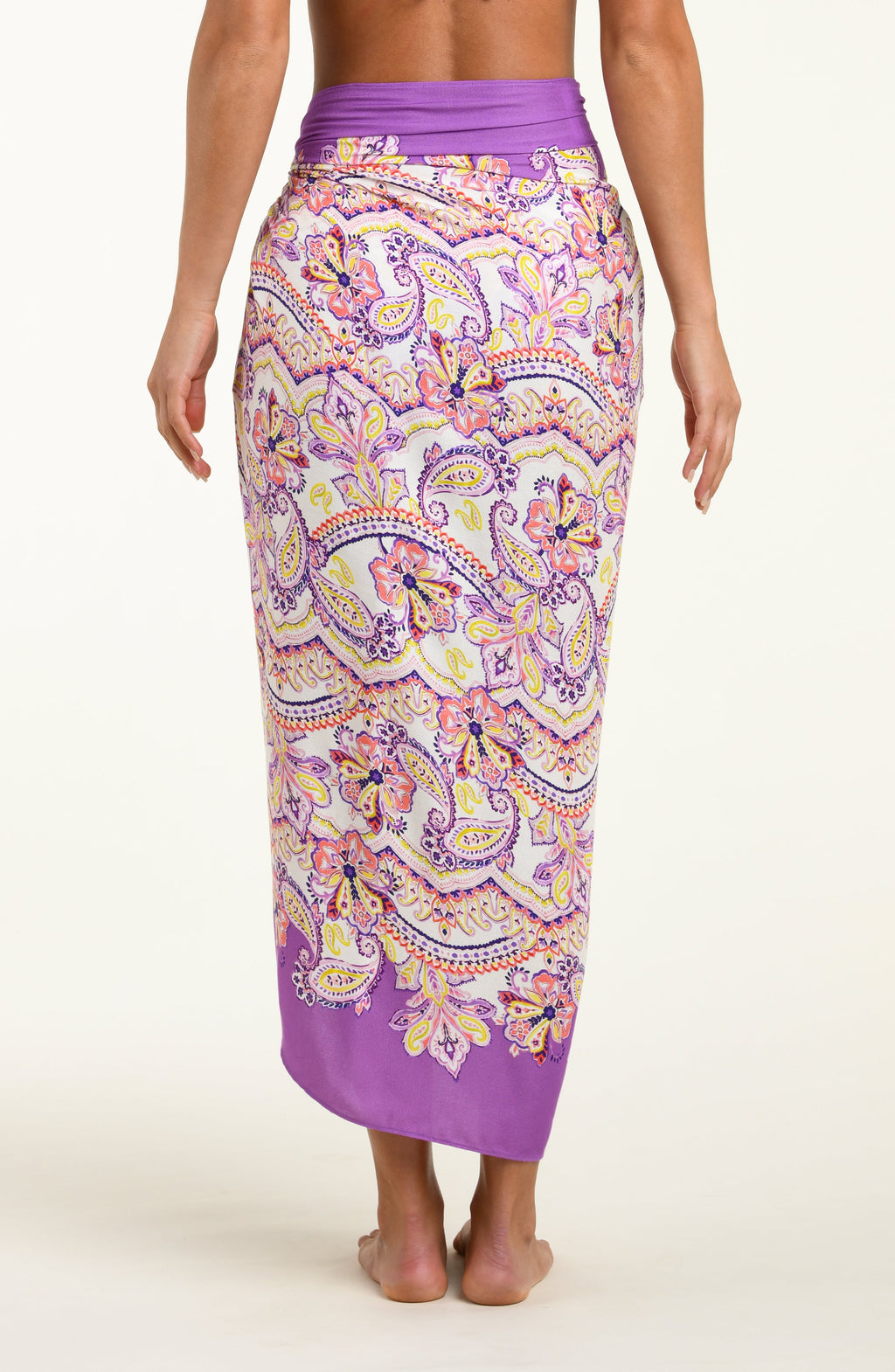 Person wearing a colorful patterned sarong with a purple top on a white background