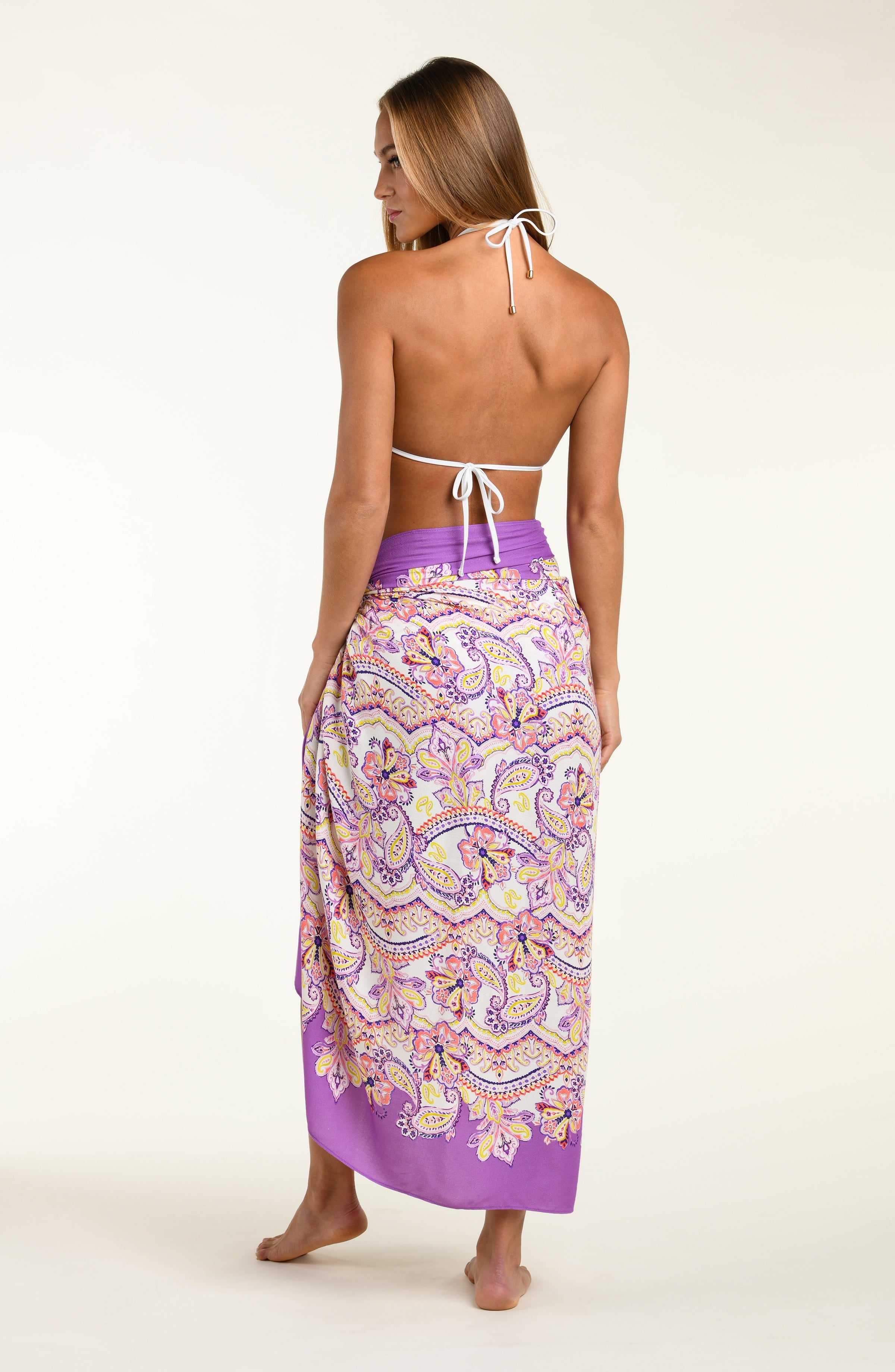 Person wearing a colorful patterned sarong with a purple top on a white background
