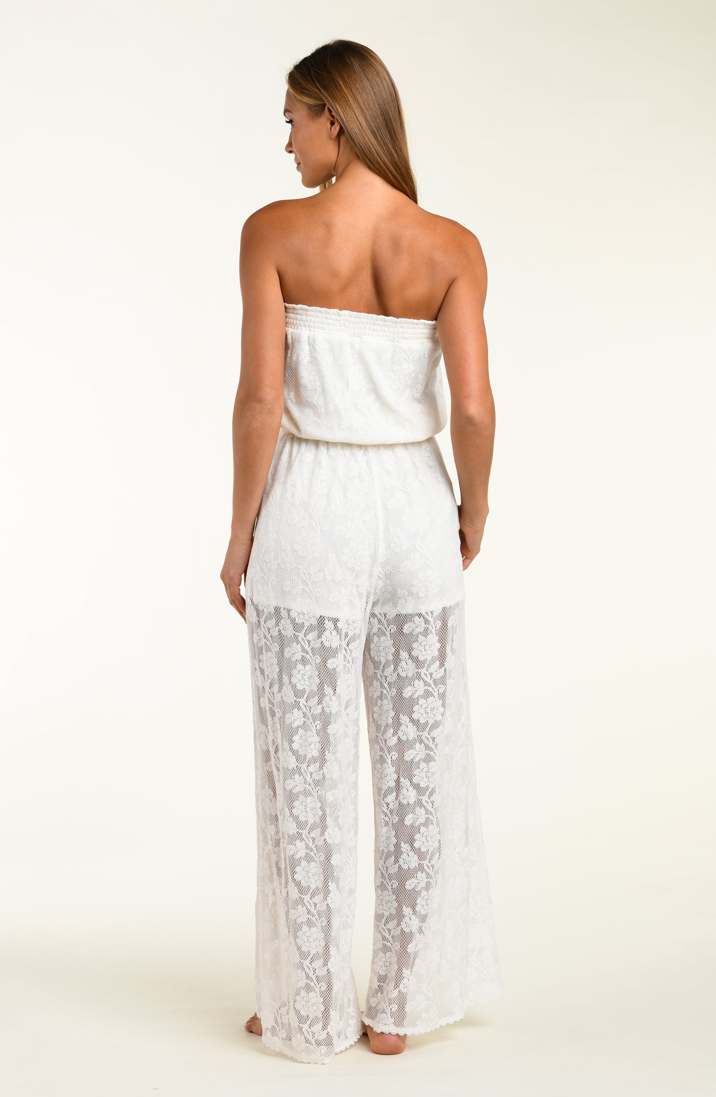 Woman wearing a white strapless jumpsuit with lace pants on a plain background