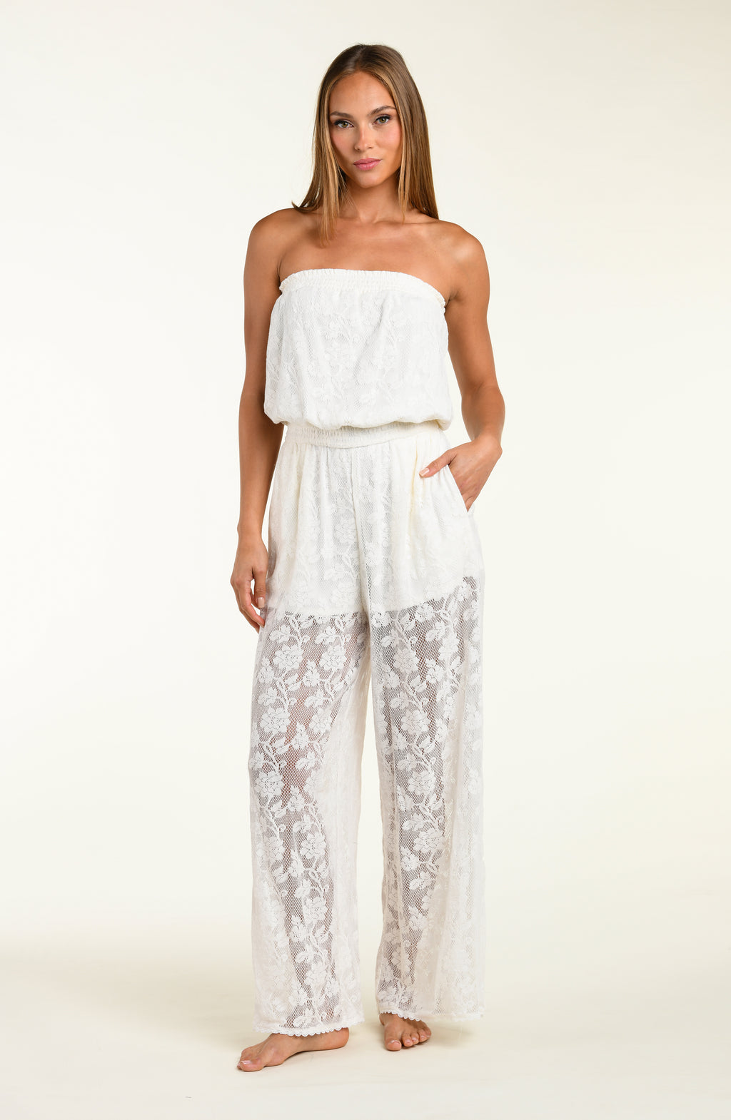 Woman wearing a white strapless jumpsuit with lace pants on a plain background