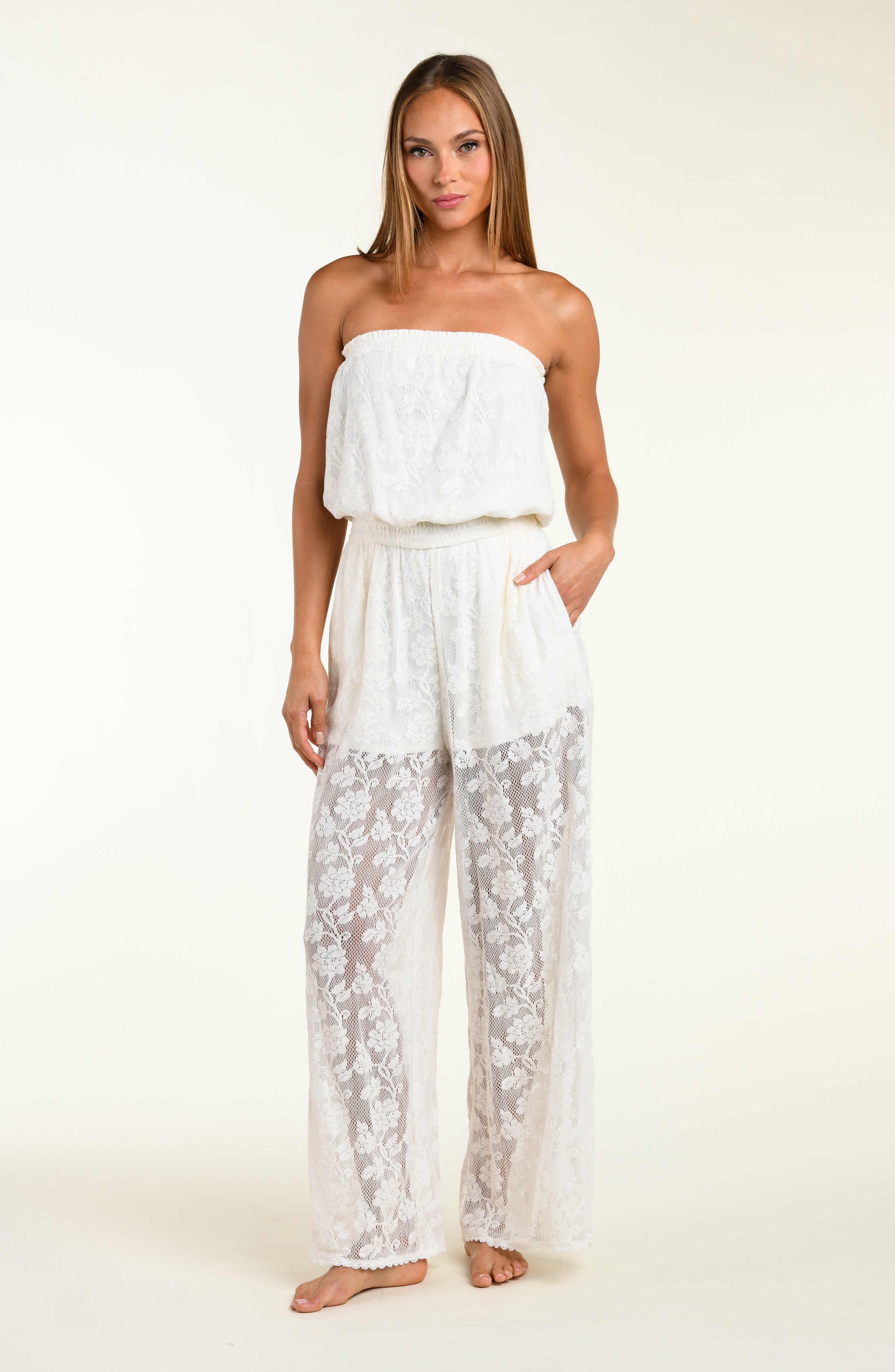 Woman wearing a white strapless jumpsuit with lace pants on a plain background