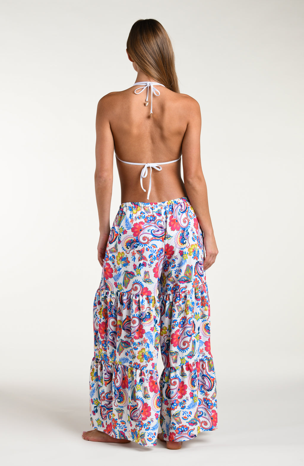 Woman wearing a multicolored bikini top and matching beach pants against a white background. 