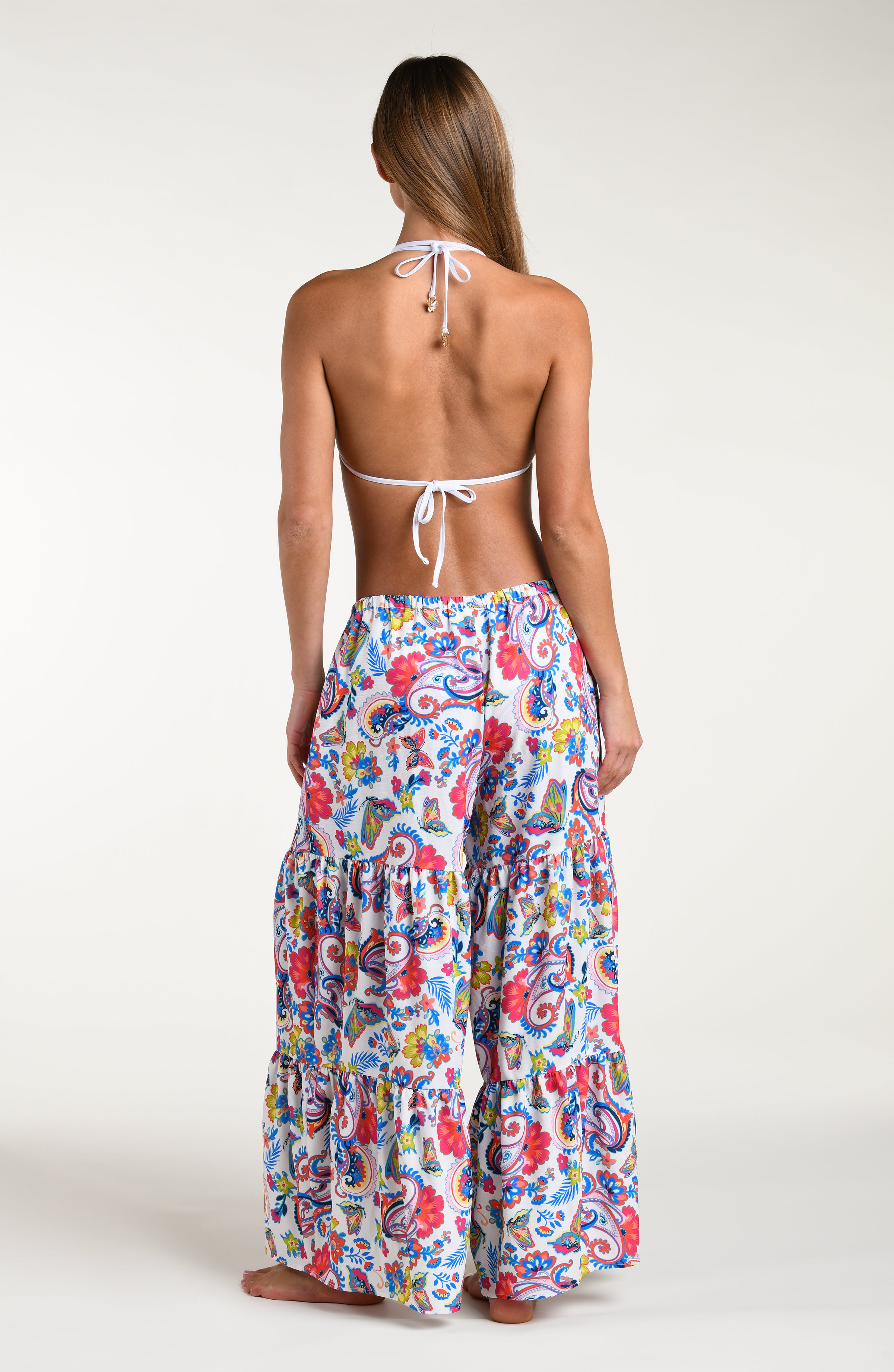 Woman wearing a multicolored bikini top and matching beach pants against a white background. 