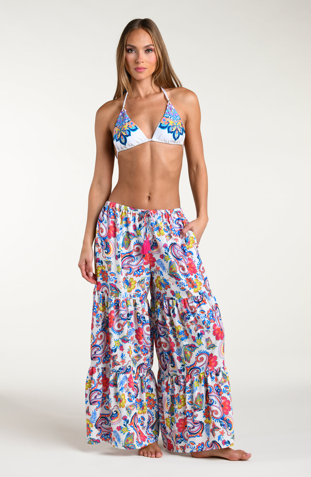 Woman wearing a multicolored bikini top and matching beach pants against a white background. 