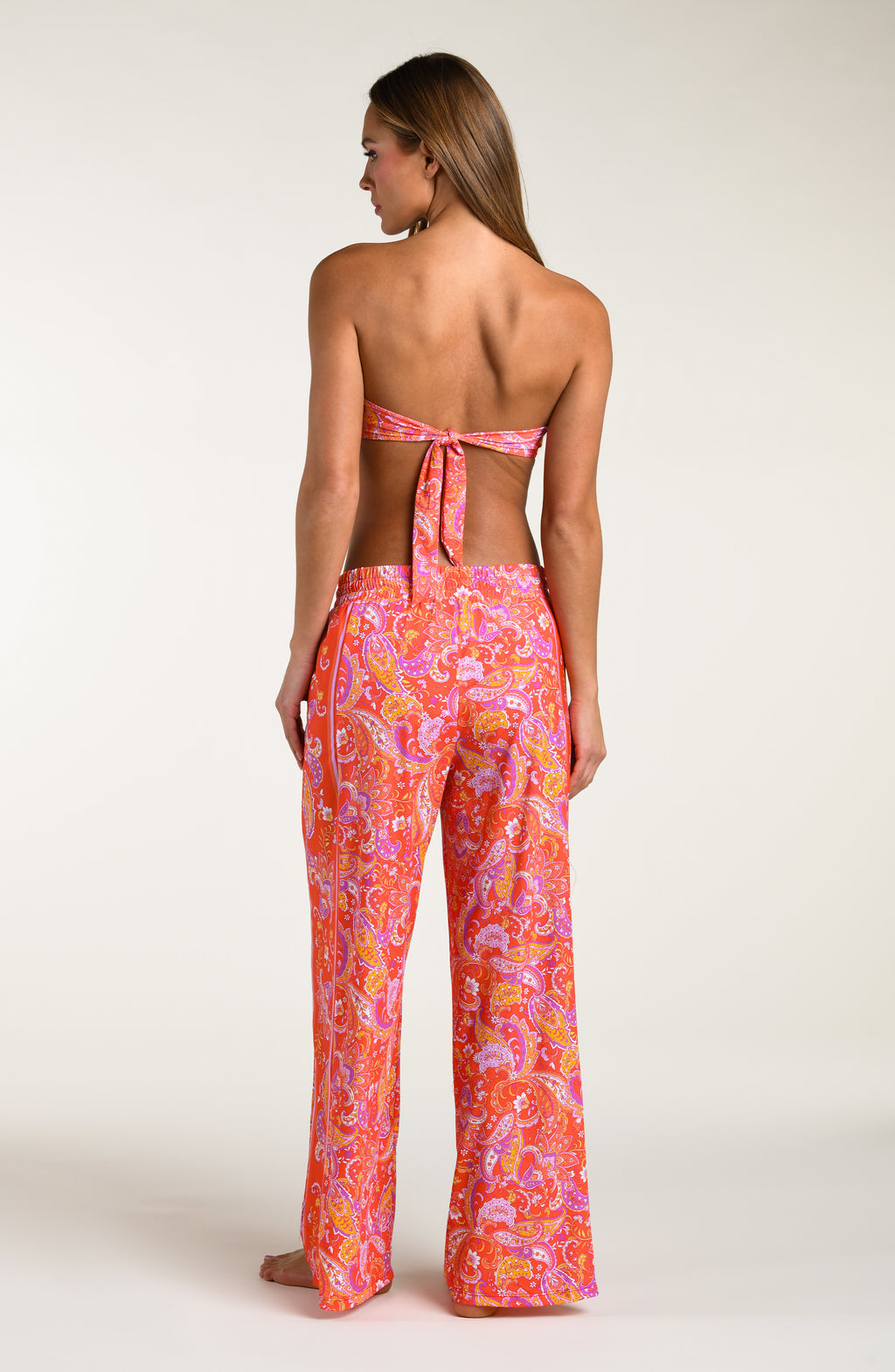 Woman wearing a pink and orange multicolored patterned bikini top and   matching pants worn by a person on a white background.