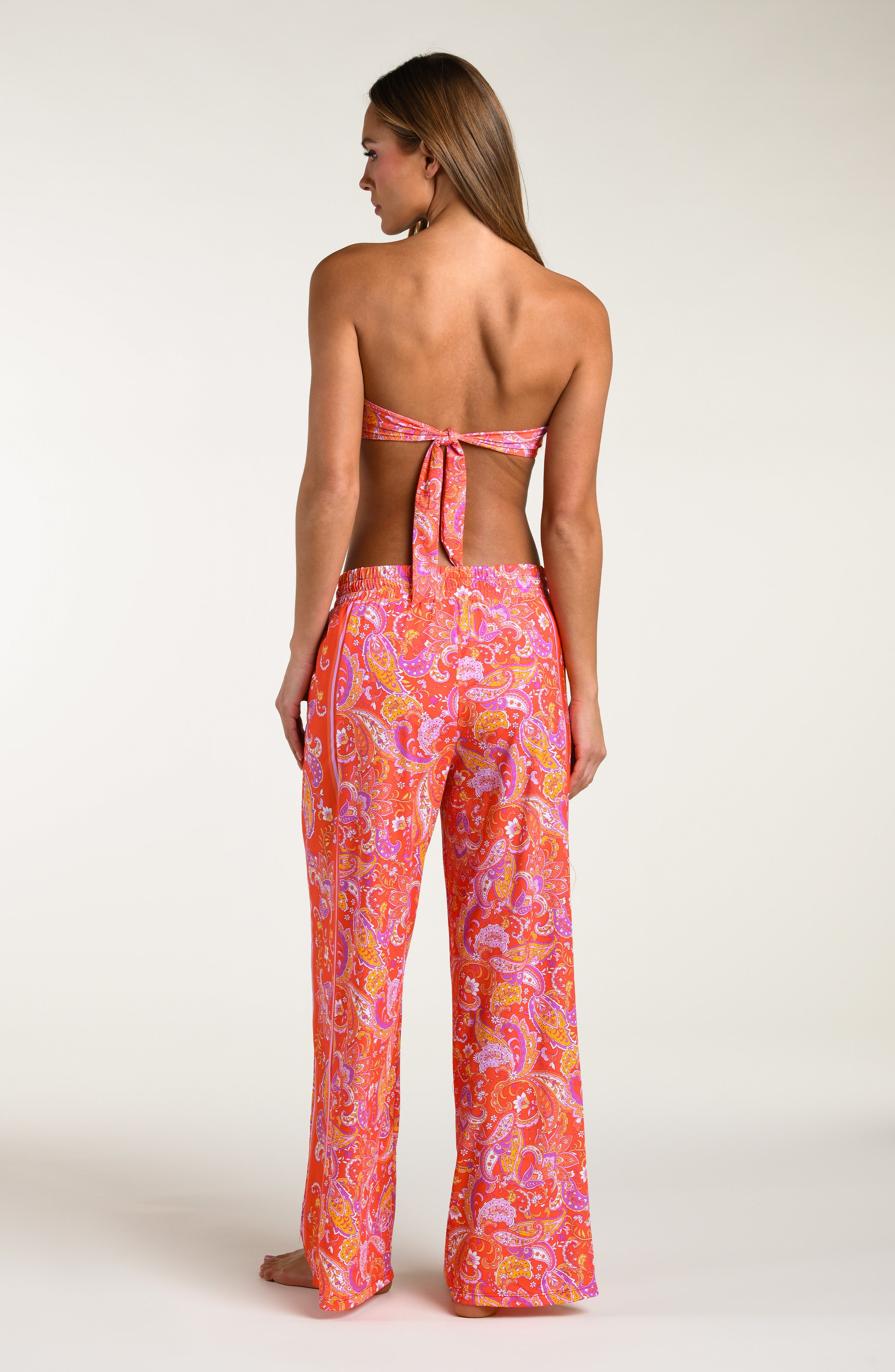 Woman wearing a pink and orange multicolored patterned bikini top and   matching pants worn by a person on a white background.
