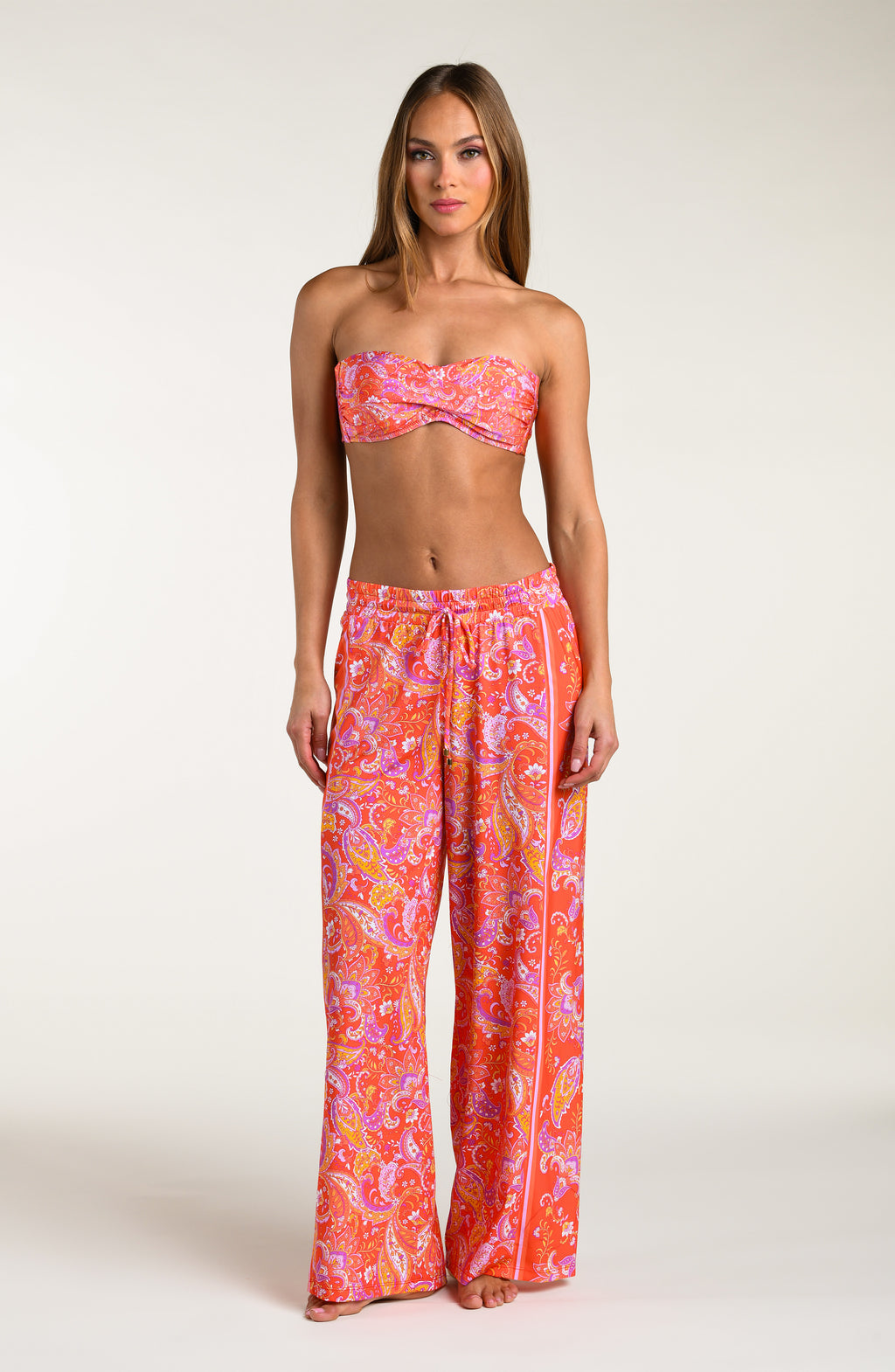 Woman wearing a pink and orange multicolored patterned bikini top and   matching pants worn by a person on a white background.