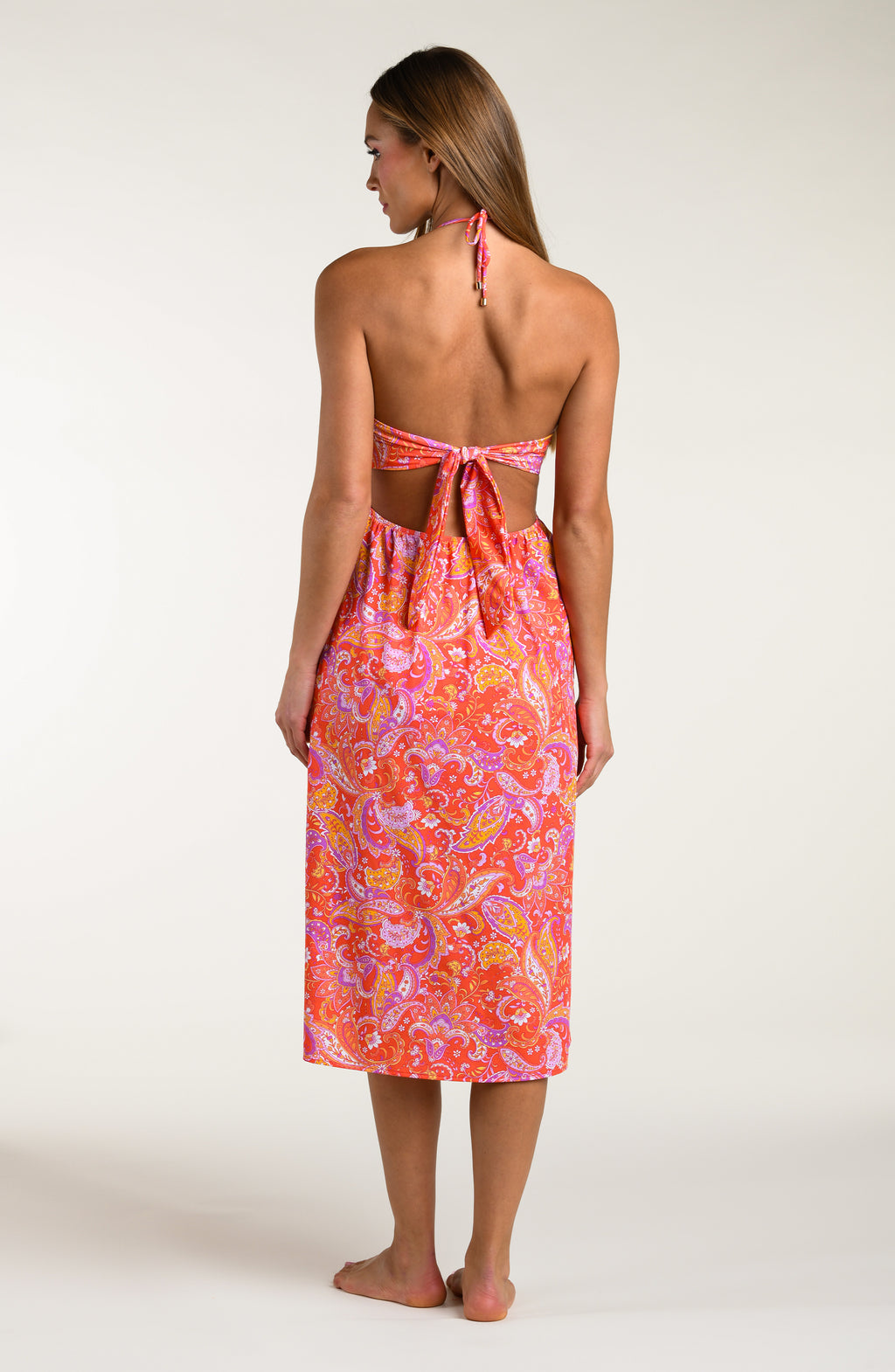 Woman wearing a pink and orange multicolored midi dress cover up against a white background.