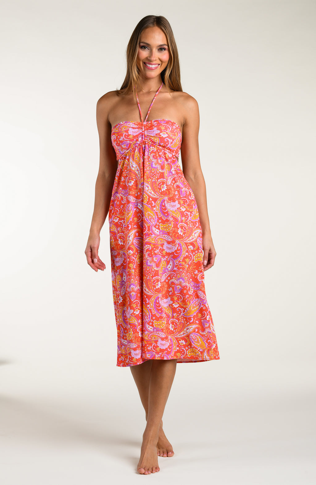 Woman wearing a pink and orange multicolored midi dress cover up against a white background.
