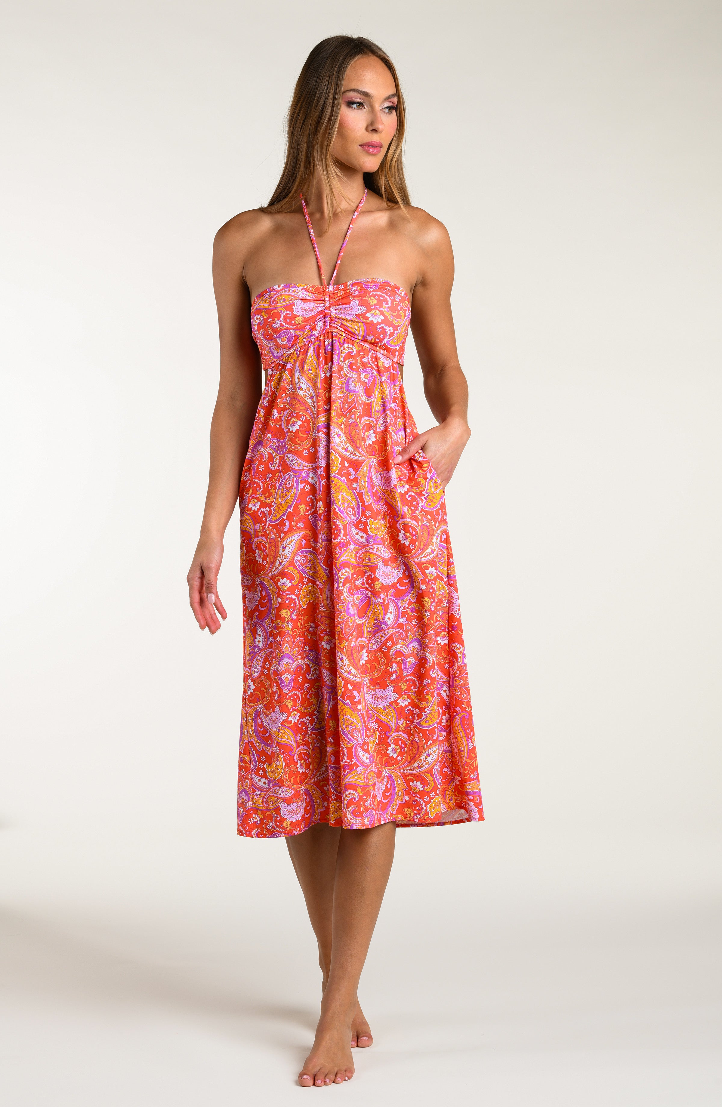 Woman wearing a pink and orange multicolored midi dress cover up against a white background.