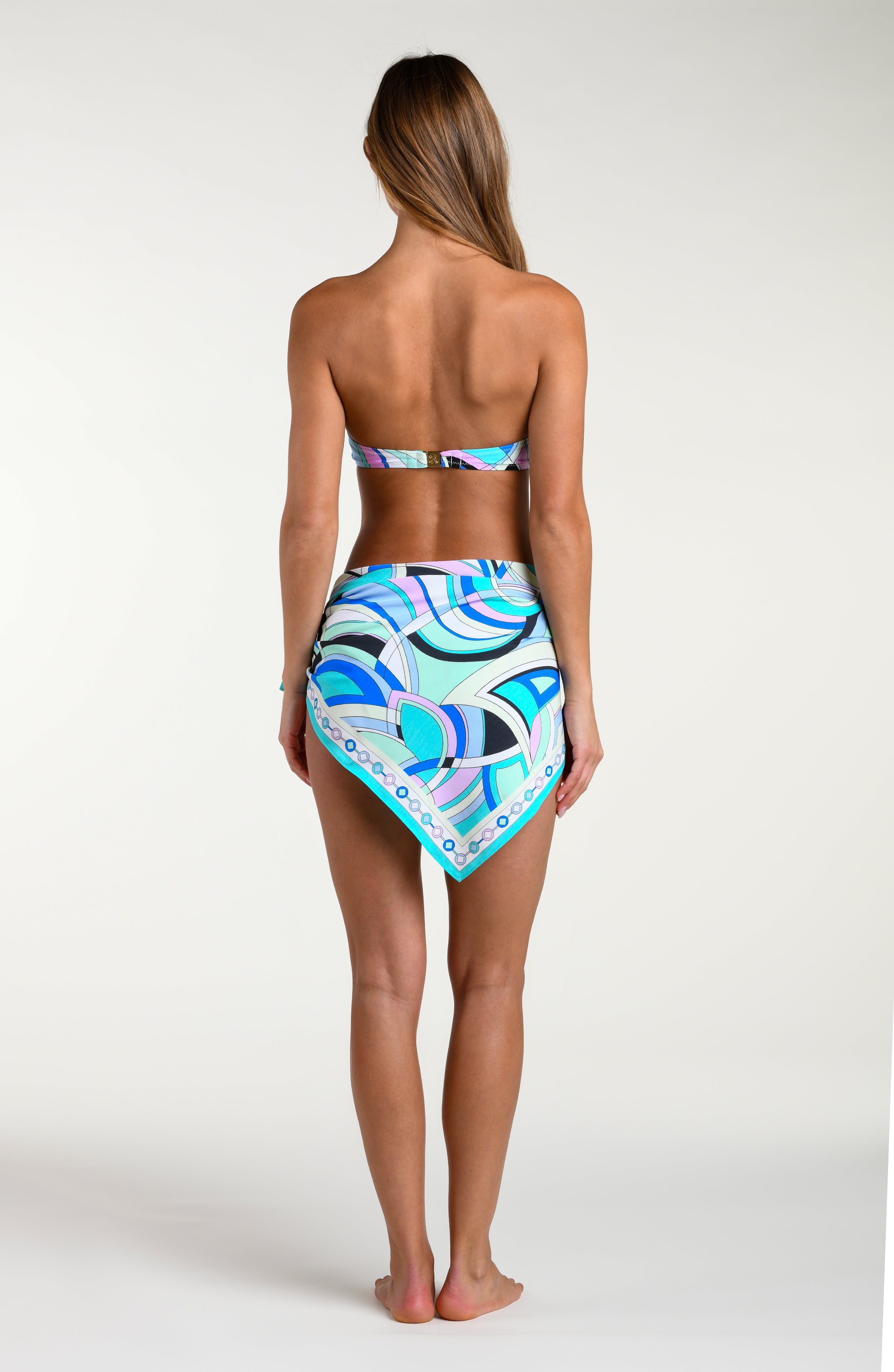 Woman wearing a multicolored bikini top and matching sarong against a white background. 