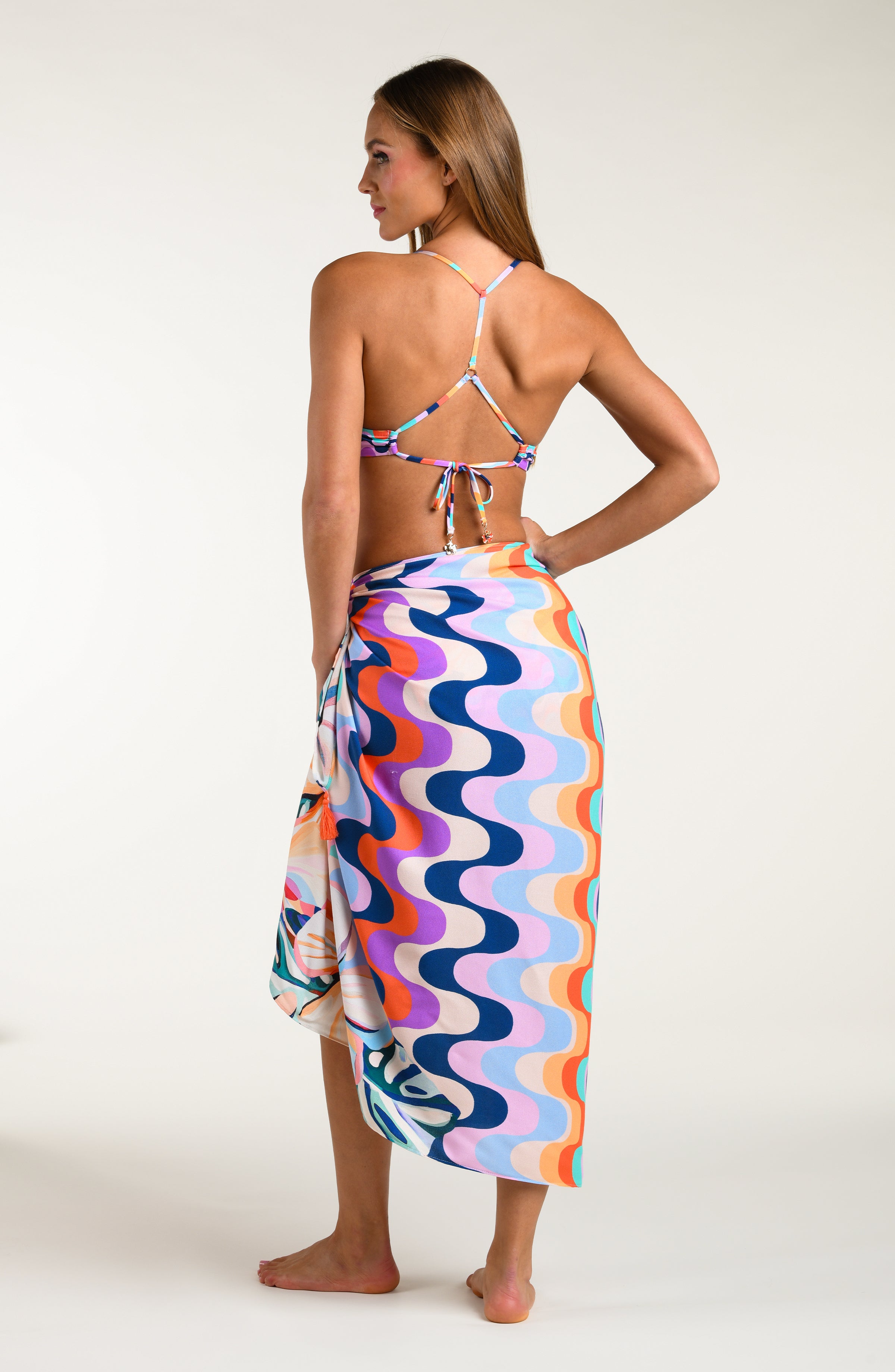 Woman wearing a multicolored patterned bikini top and matching sarong on a white background