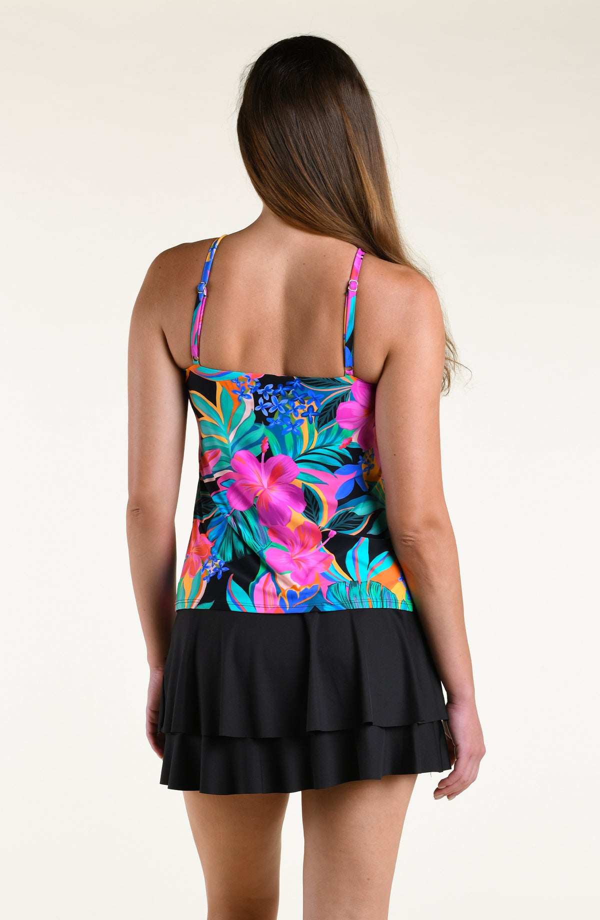 Woman wearing a bright multicolored high neck tankini top and solid black swim skirt against a white background. 