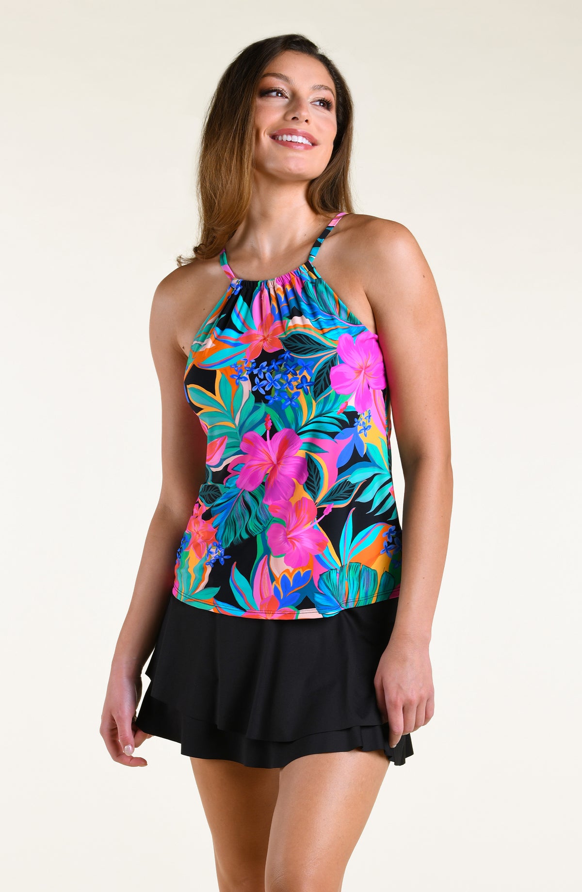 Woman wearing a bright multicolored high neck tankini top and solid black swim skirt against a white background. 