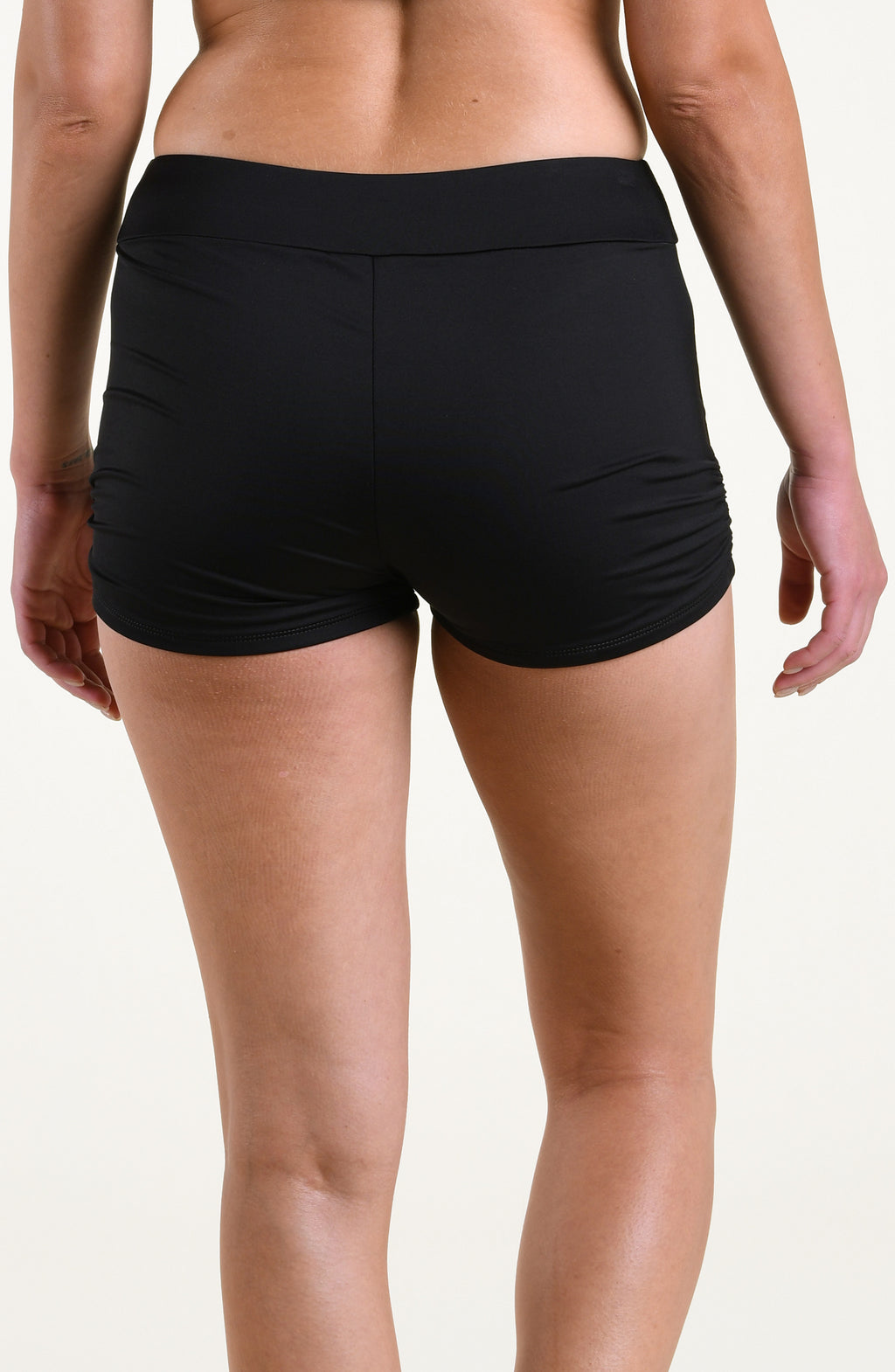 Woman wearing solid black swim shorts against a white background. 