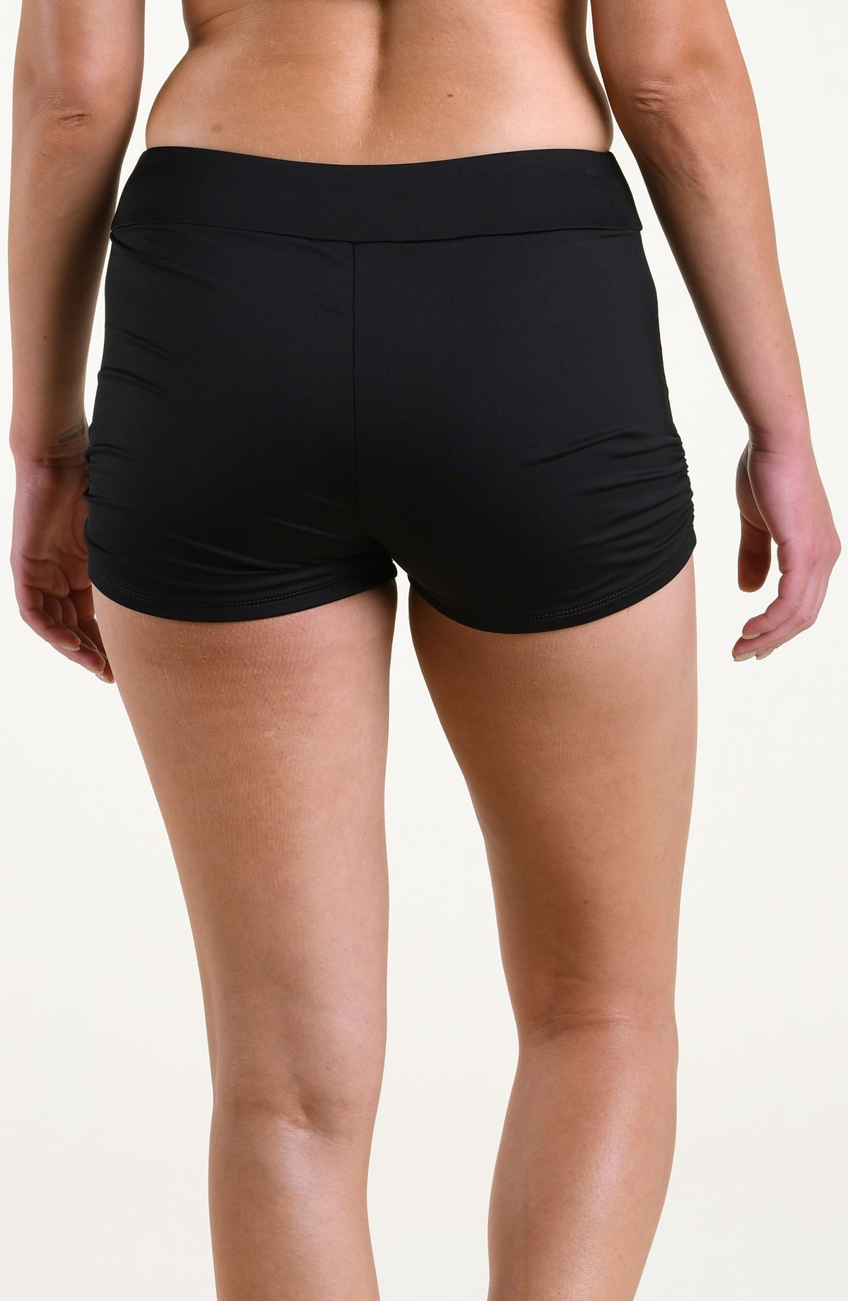 Woman wearing solid black swim shorts against a white background. 