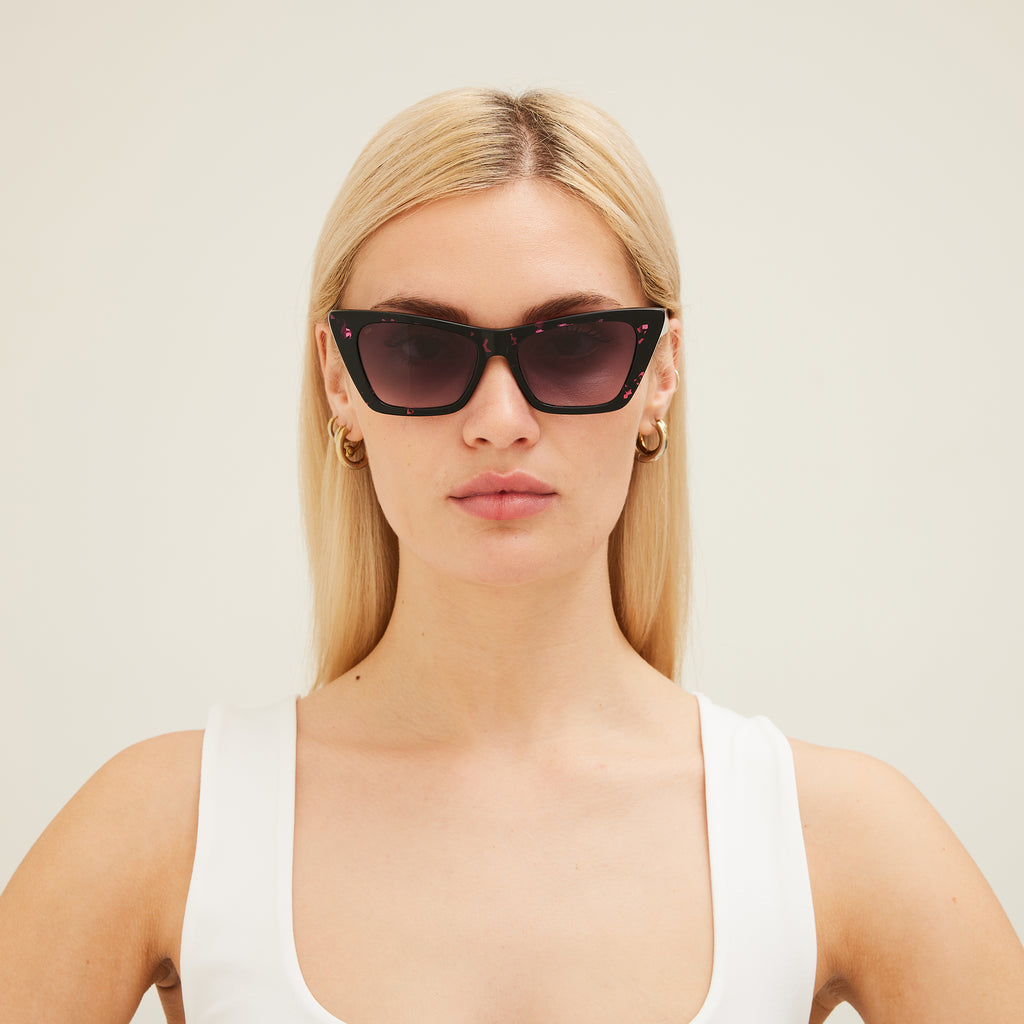 Woman wearing black cat-eye sunglasses with pink patterns on a white background