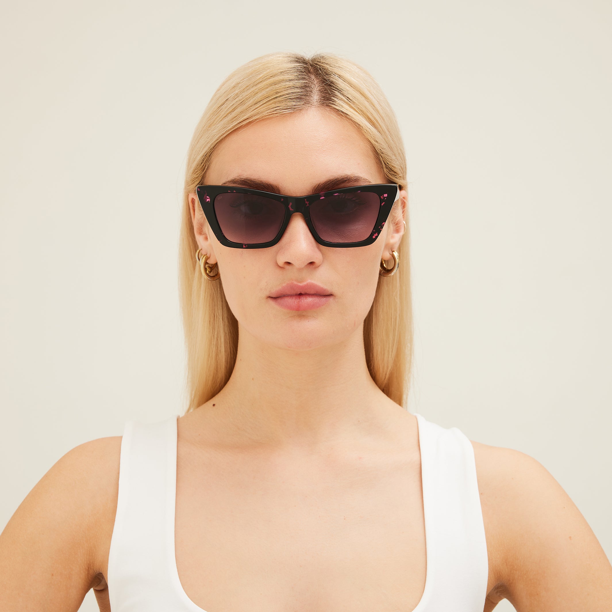 Woman wearing black cat-eye sunglasses with pink patterns on a white background