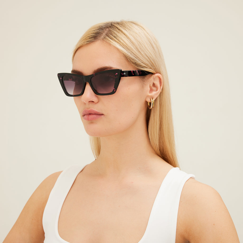 Woman wearing black cat-eye sunglasses with pink patterns on a white background