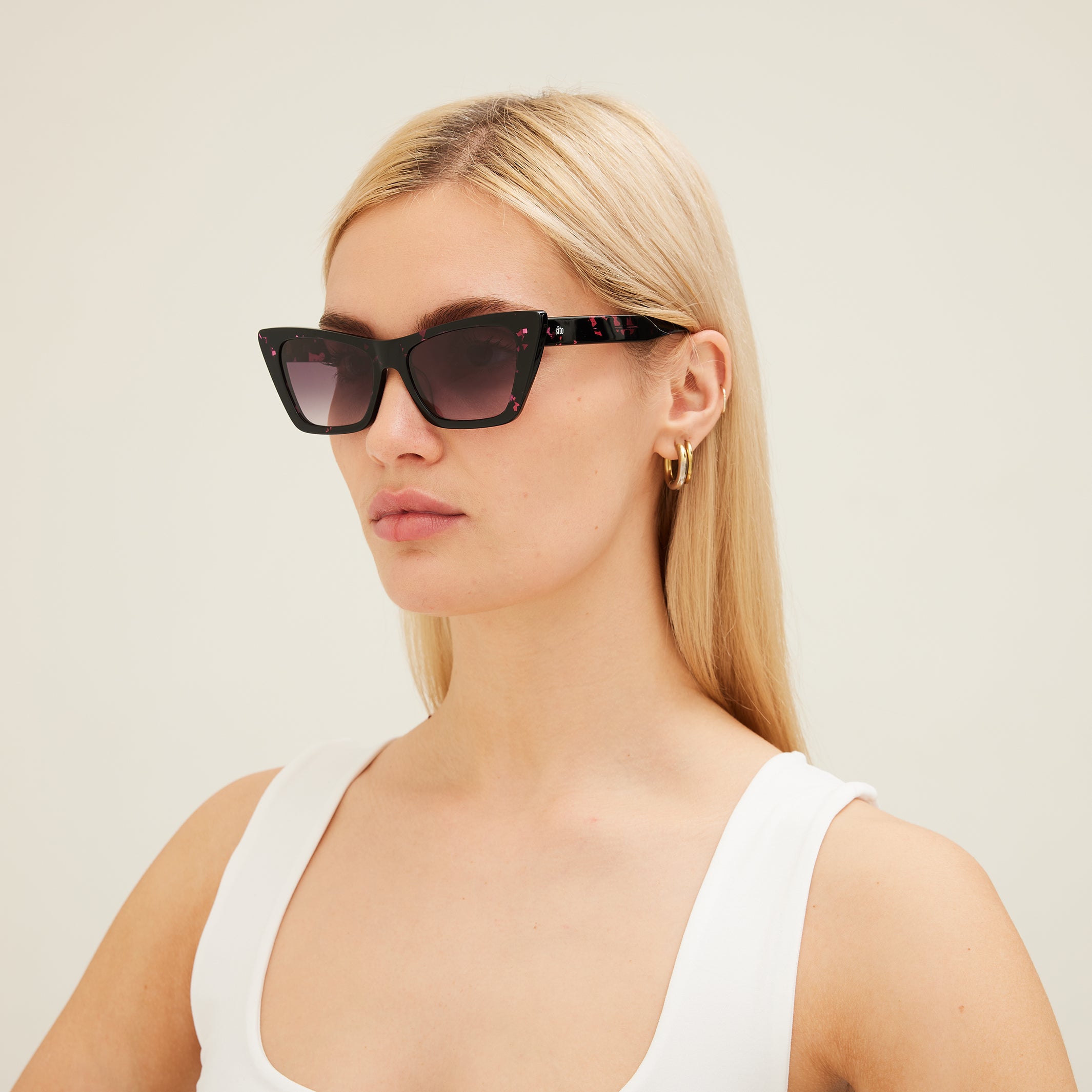 Woman wearing black cat-eye sunglasses with pink patterns on a white background