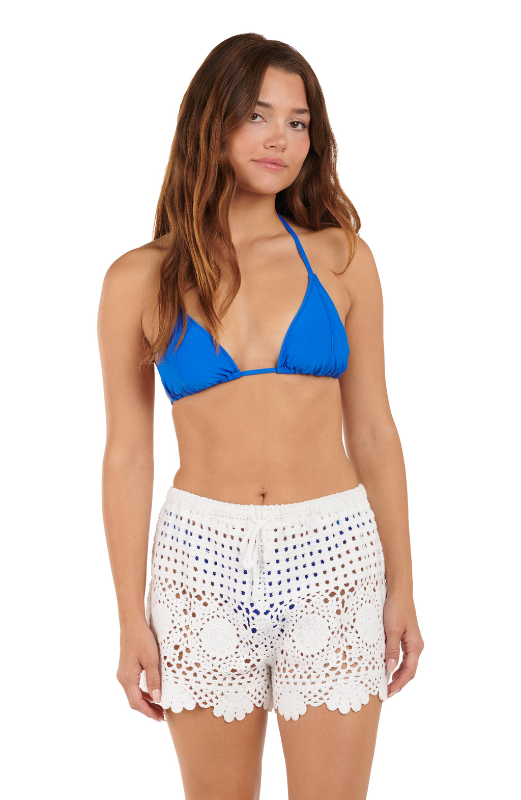 Woman wearing a blue bikini top and white crochet shorts on a white background