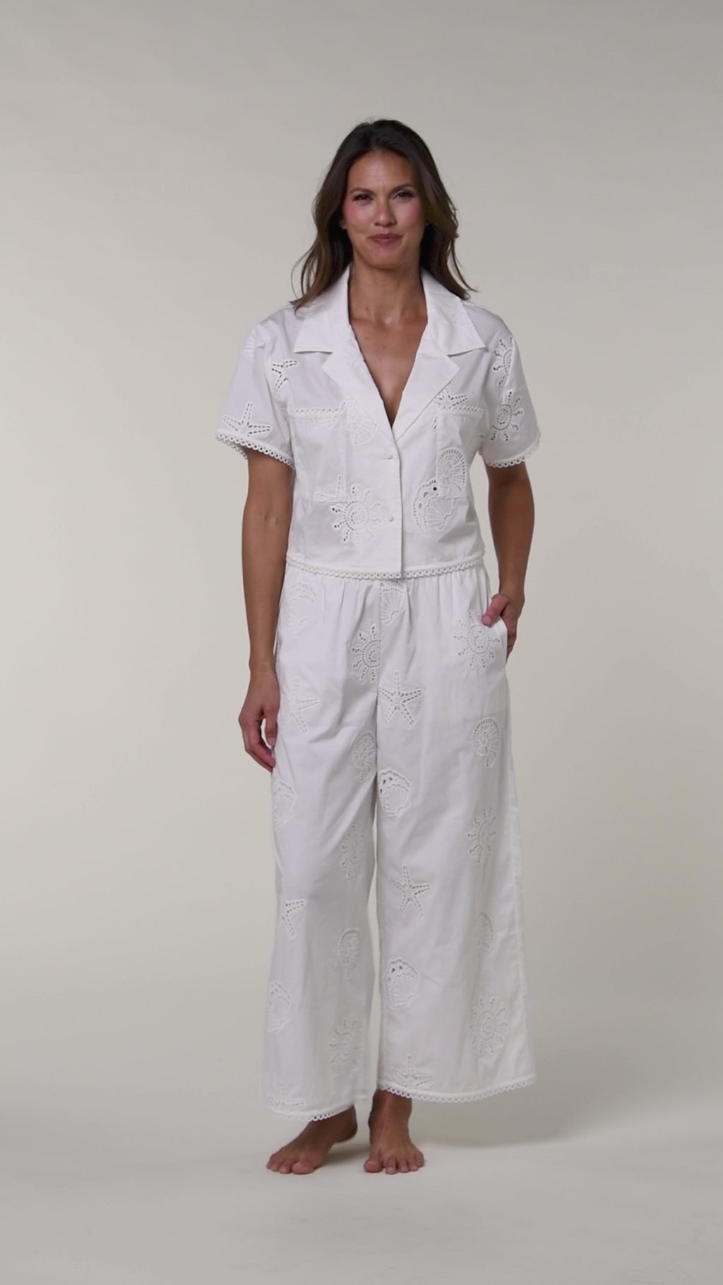 Video of a woman wearing a white cover up shirt with matching pants against a white background.