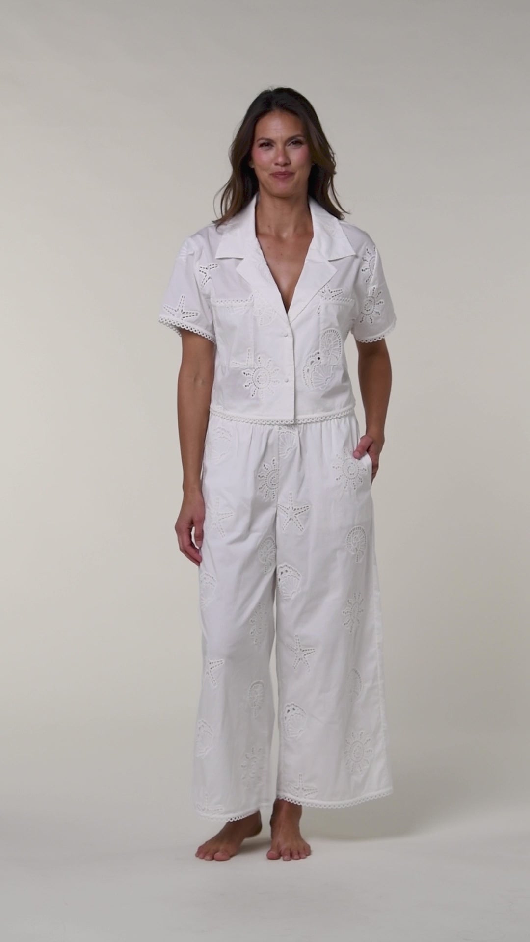 Video of a woman wearing a white cover up shirt with matching pants against a white background.