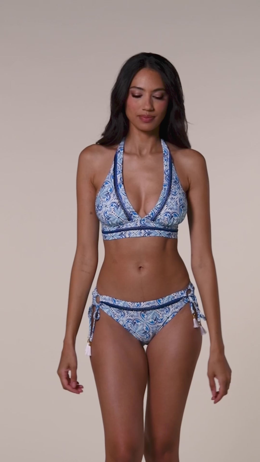 Video of a woman wearing a blue patterned bikini top and matching bottom against a beige background.
