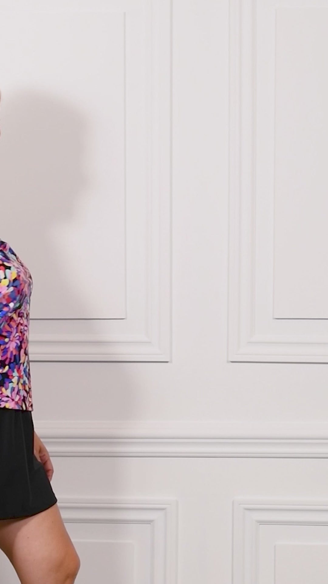 Video of a woman wearing a colorful floral tankini top and black swim skirt bottom against a white background.