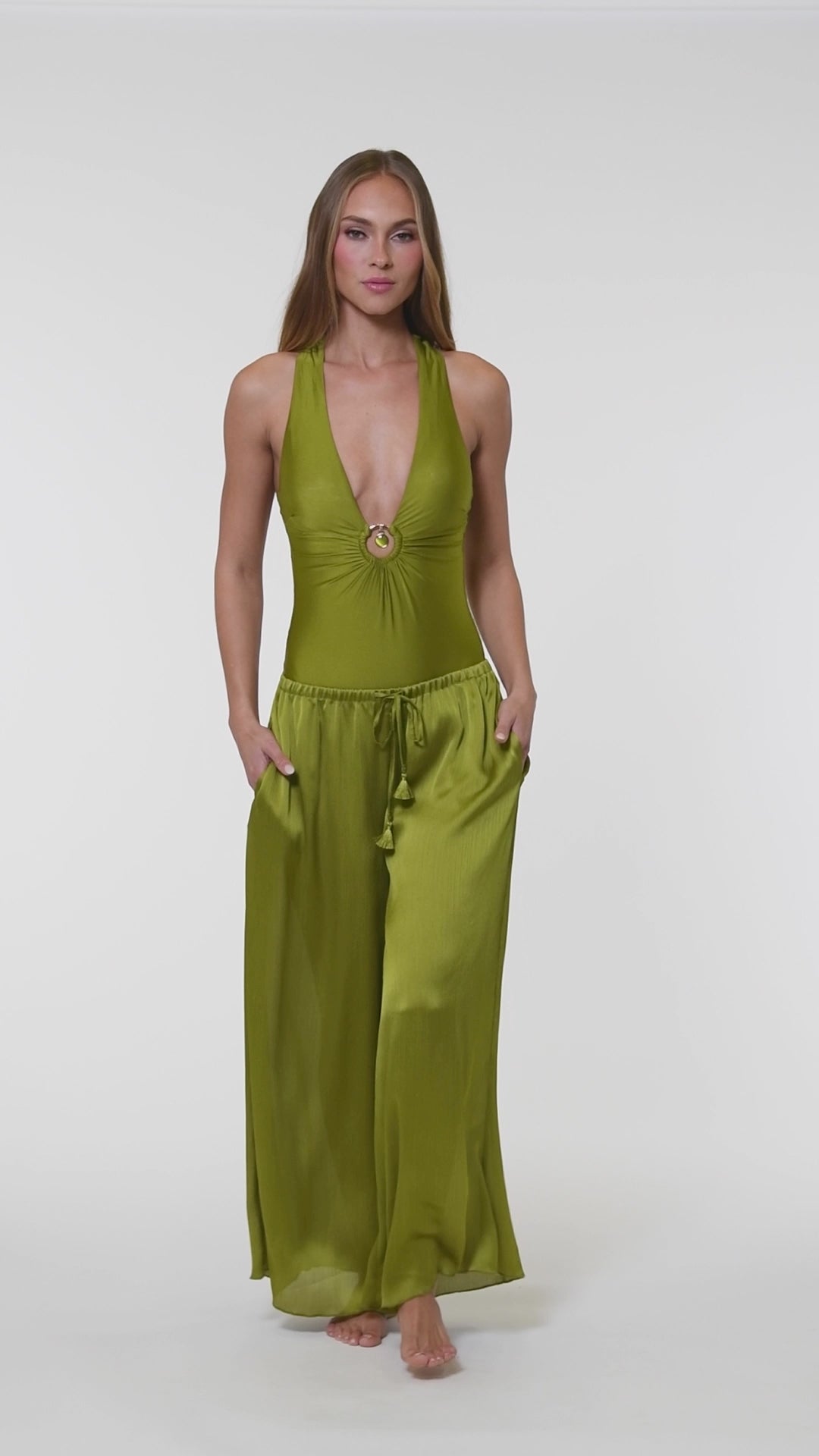 Video of a woman wearing an olive green one piece and matching pants against a white background