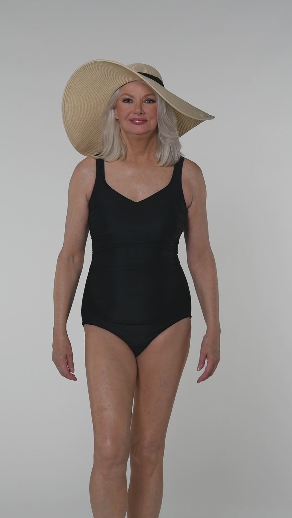 Video of a woman in an indigo one piece swimsuit against a white background. 