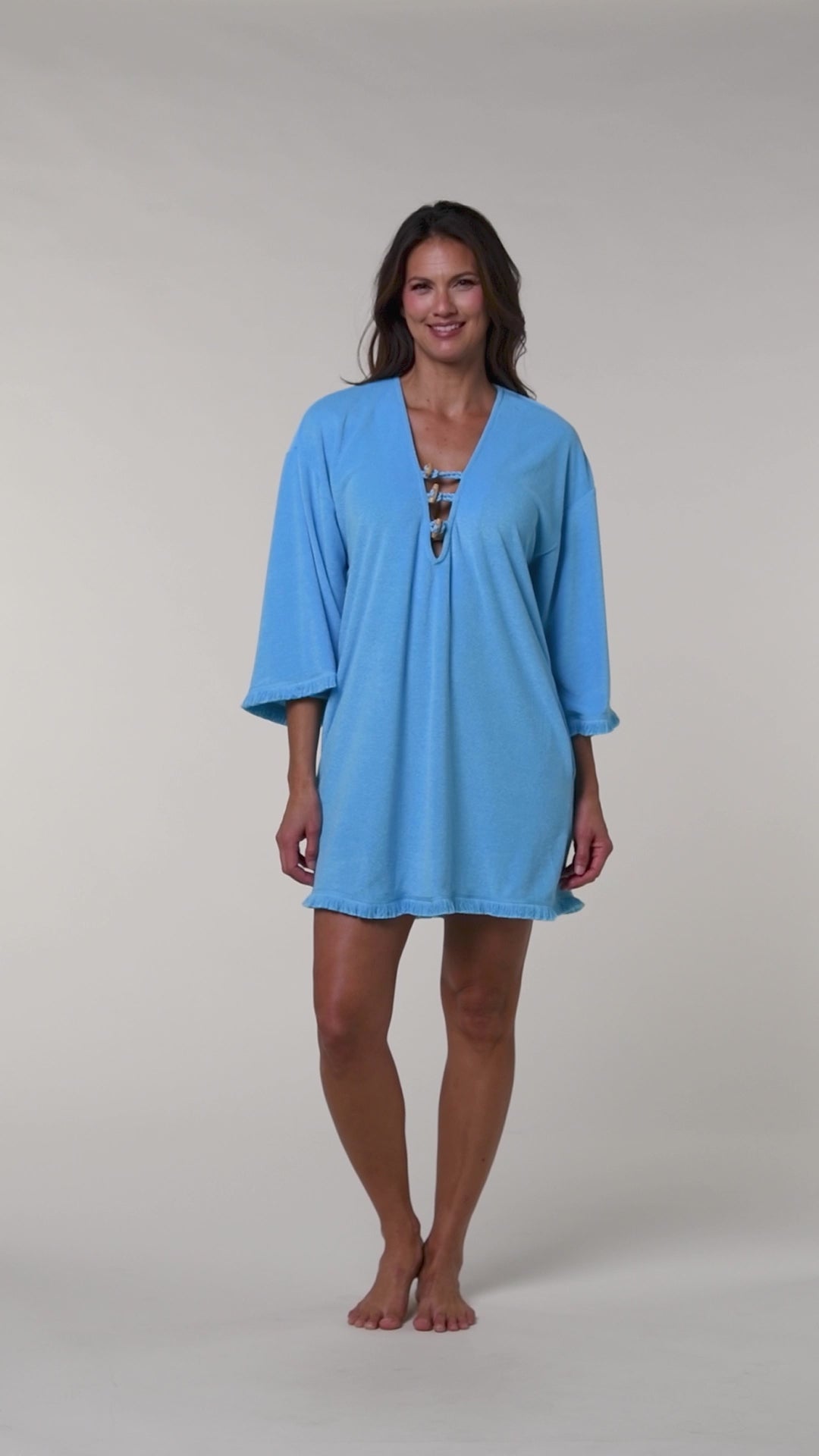 Video of a woman wearing a blue cover-up tunic on a beige background