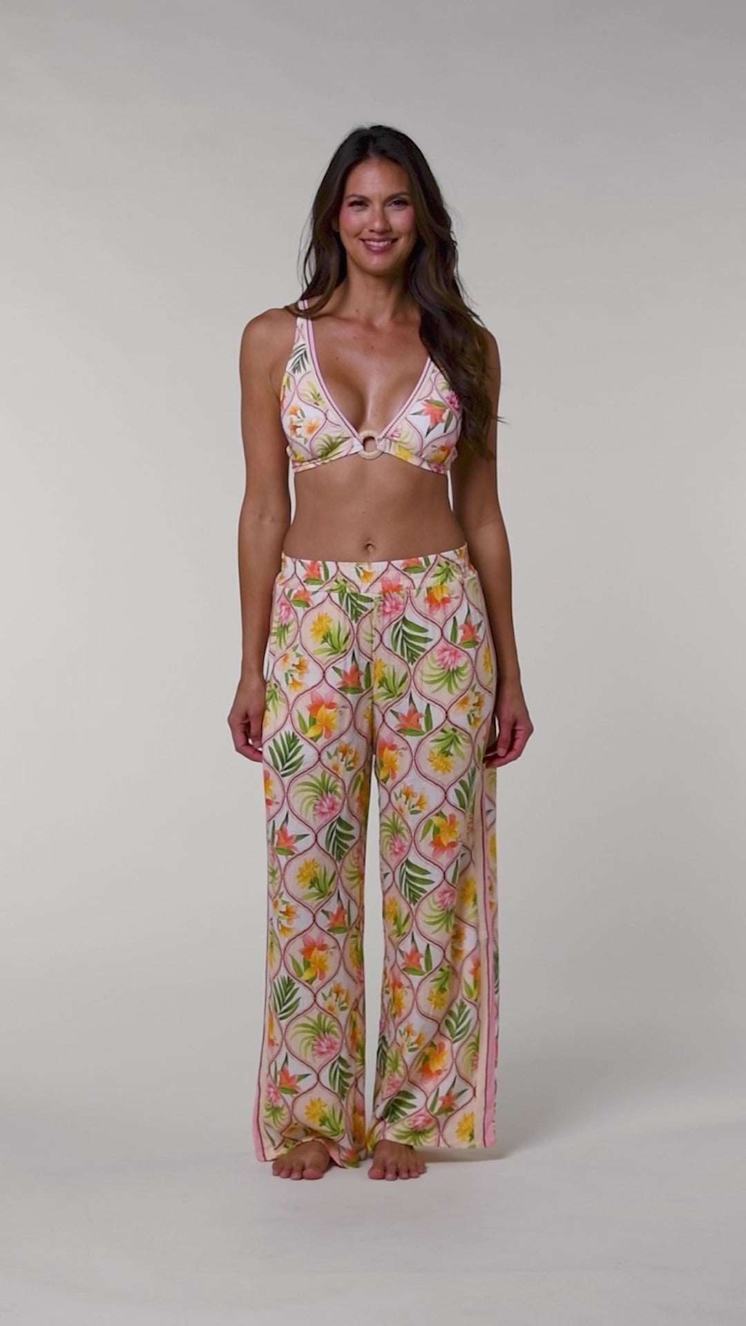 Video of a woman wearing a multicolored floral bikini top and matching pants against a white background.