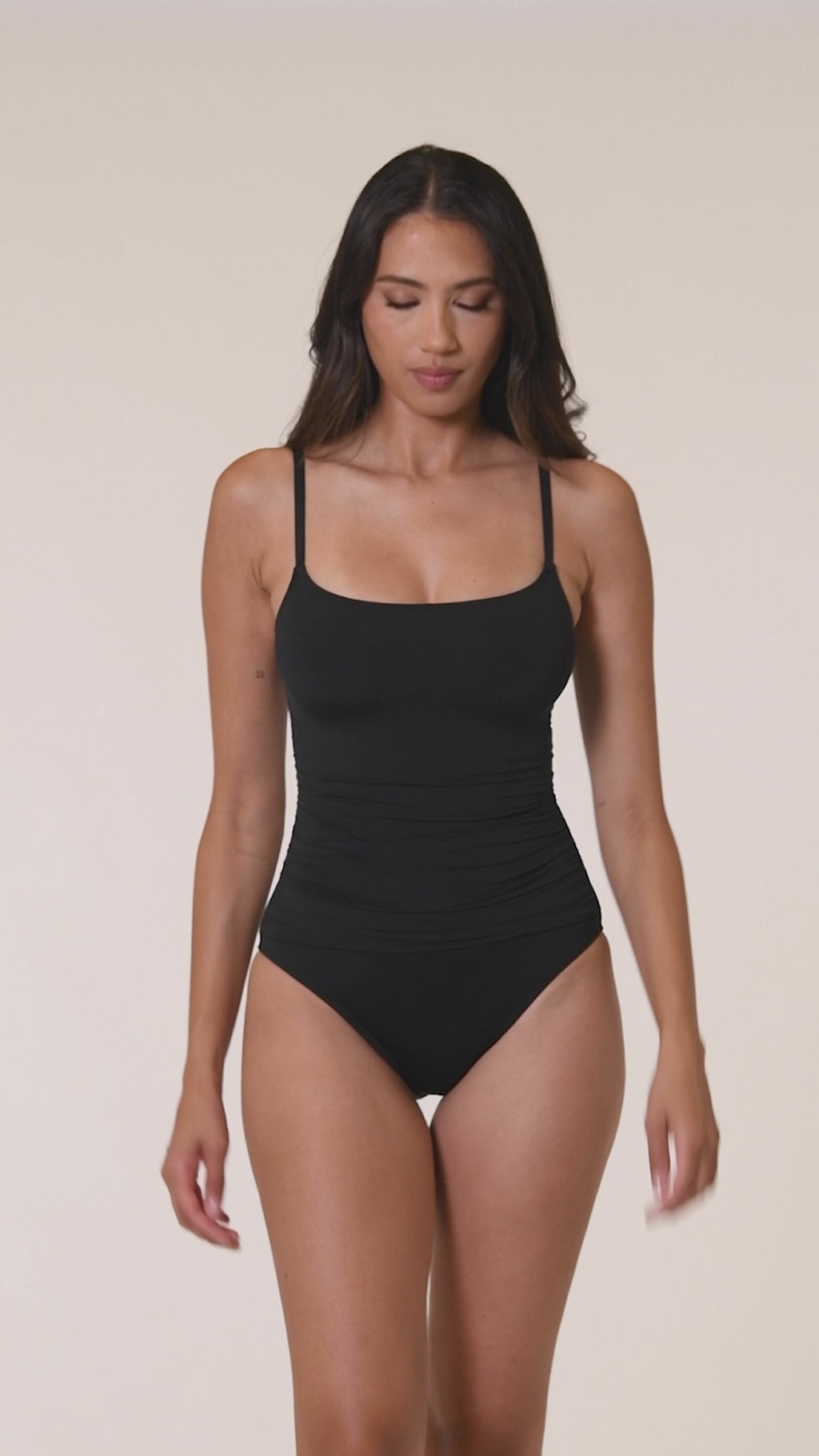 Video of a woman wearing a black swimsuit against a white background