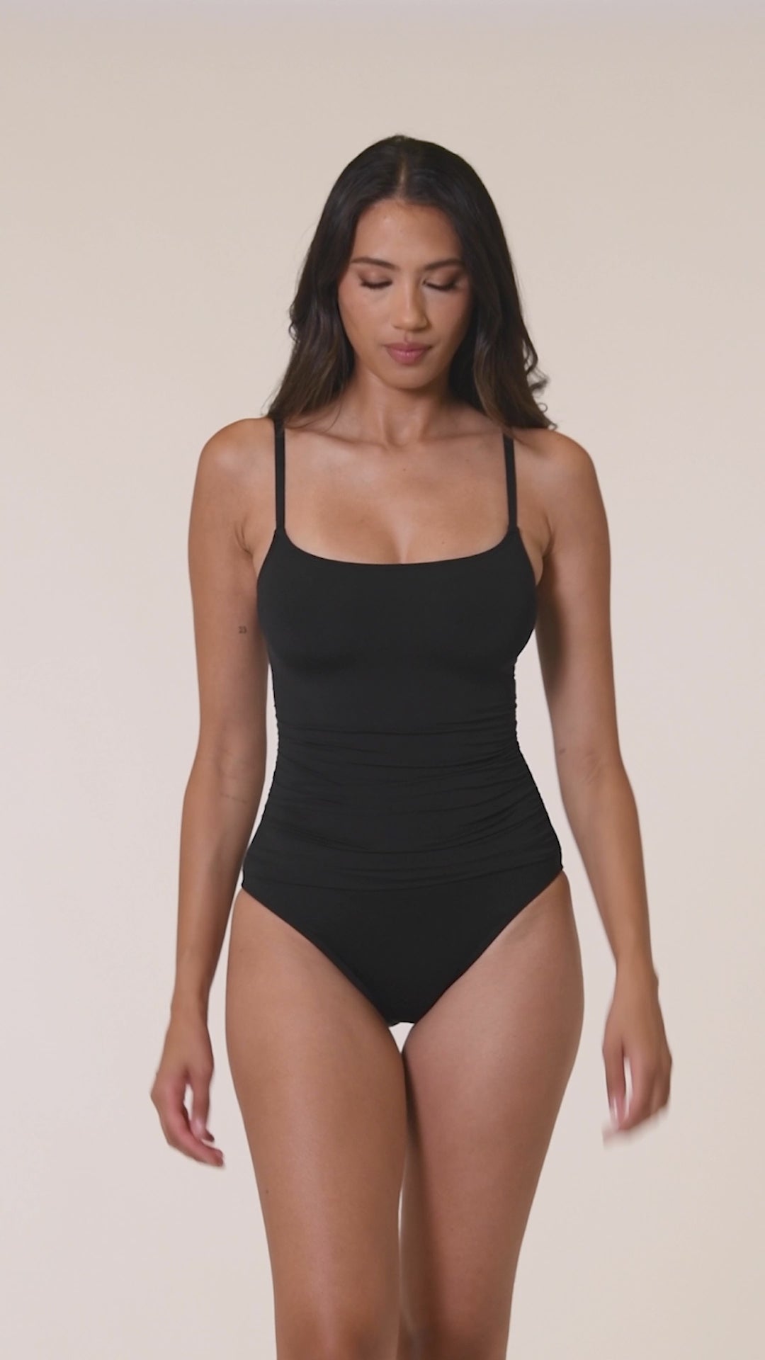 Video of a woman wearing a black swimsuit against a white background